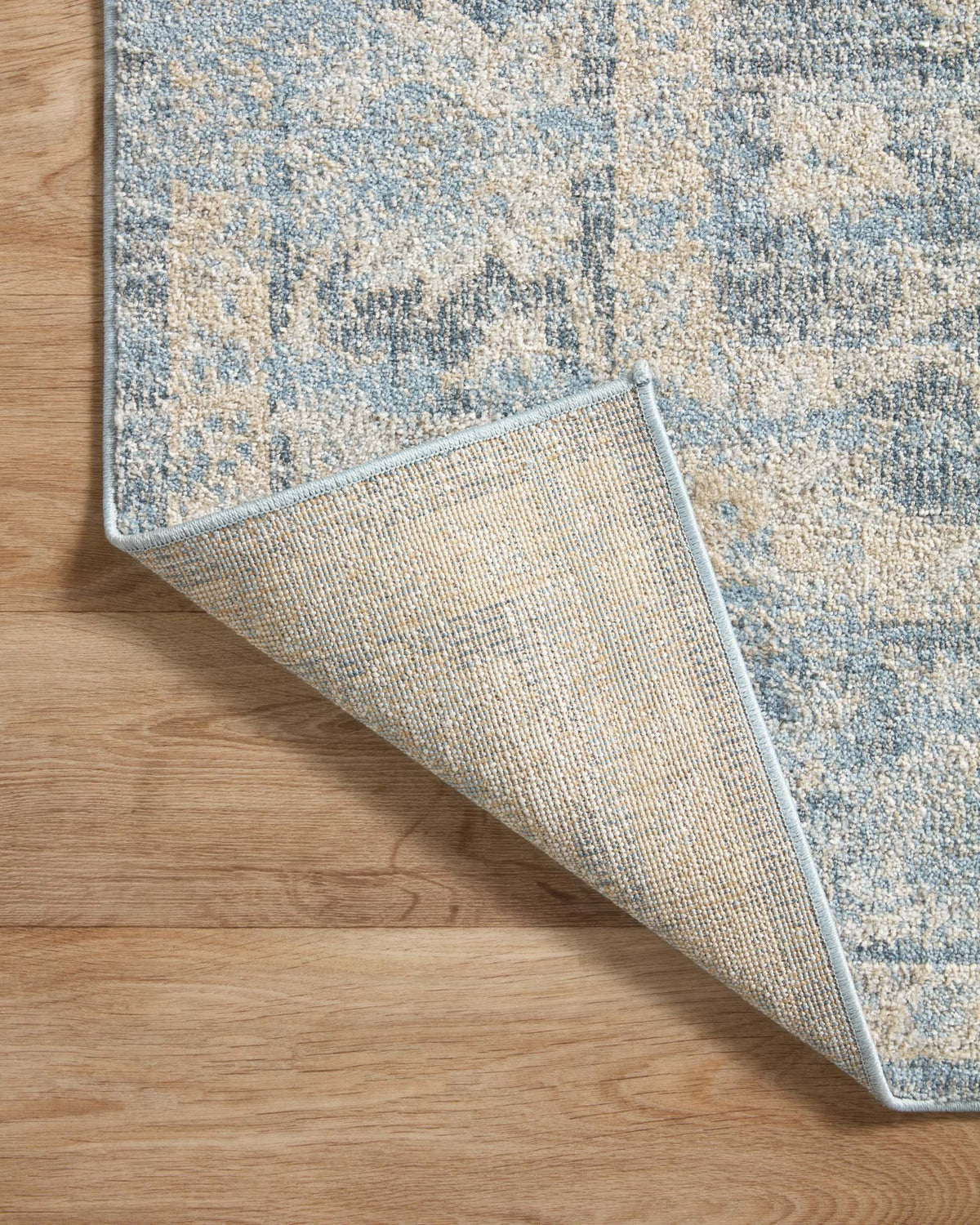 Sky blue and beige area rug with light woven underside visible at lifted corner