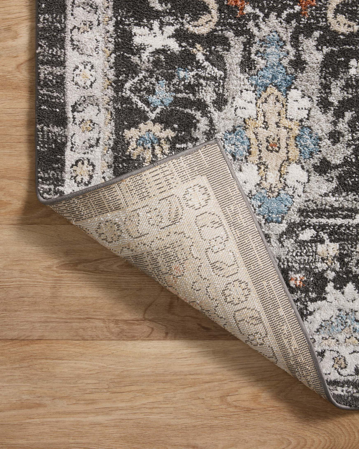 Reversed corner view of charcoal rug with woven texture and dark edge binding.
