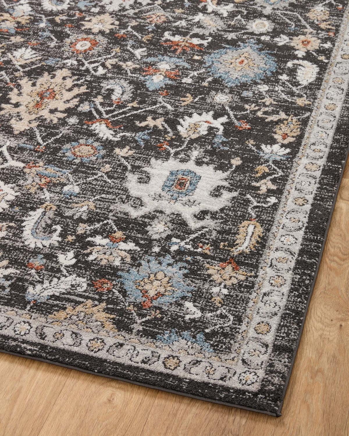 Charcoal traditional area rug angled view with scattered multicolor motifs and border trim