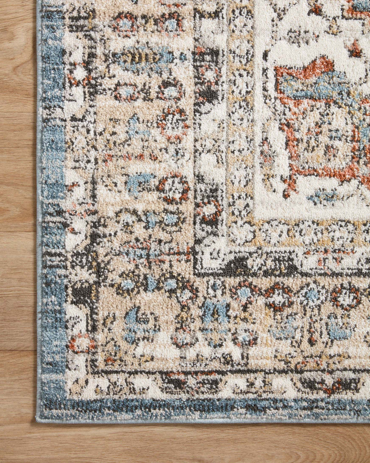 Traditional area rug border detail in sky blue, cream, and orange with distressed motifs