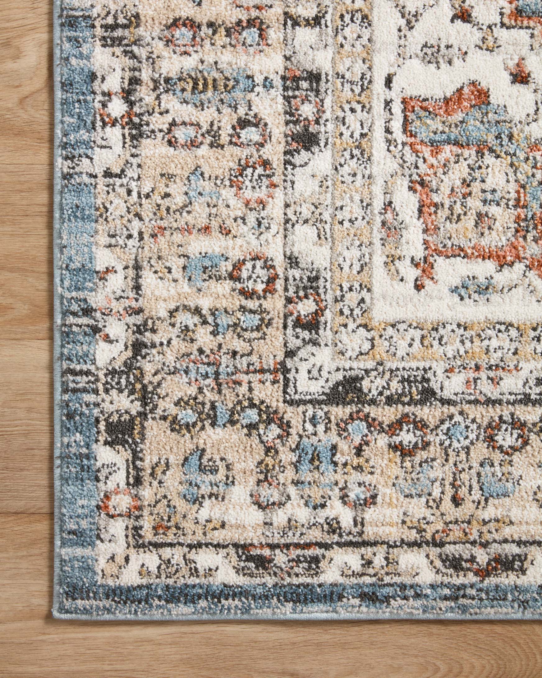 Corner view of traditional round rug with cream field, sky blue tones, and rust accents