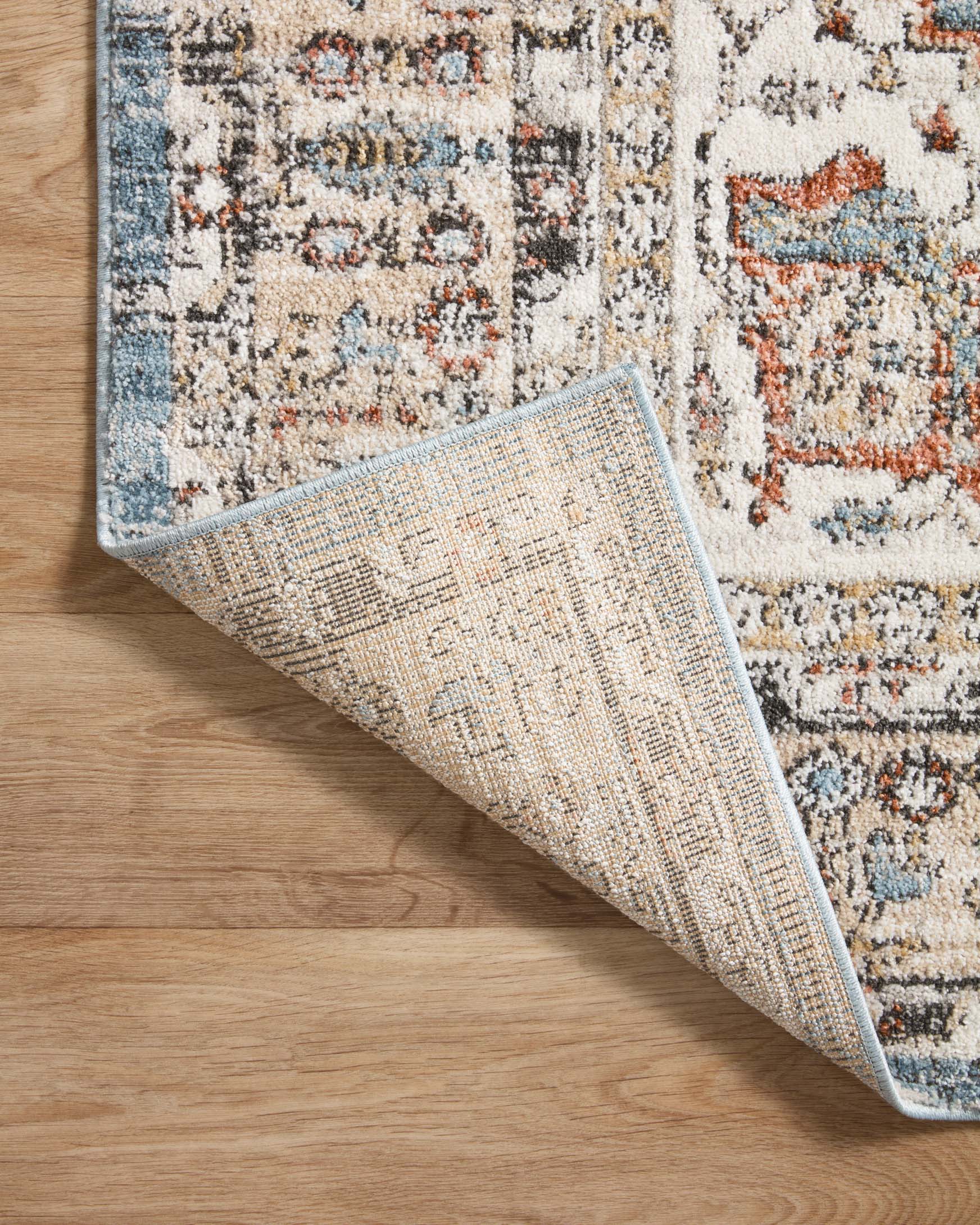 Traditional accent rug edge detail on wood floor, showing woven texture and speckled pattern