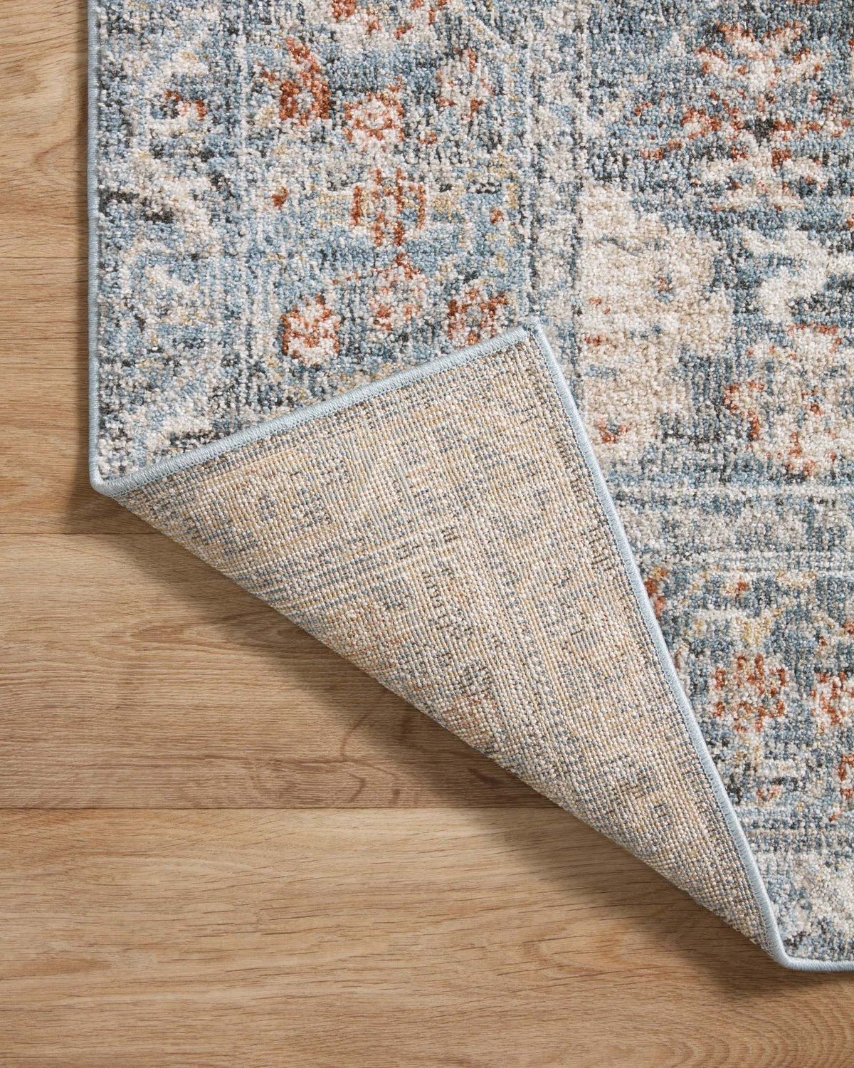 Rug corner with visible underside: sky blue pattern with rust-orange flecks, bound edge