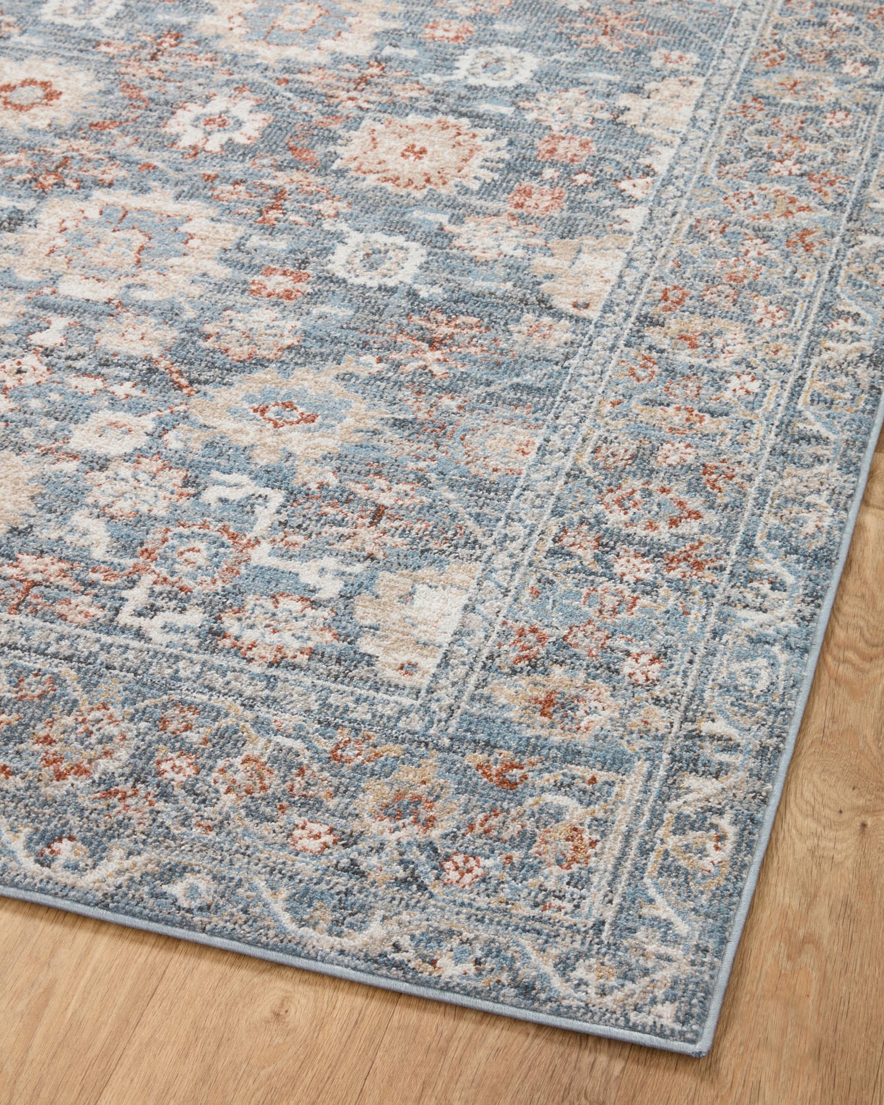 Traditional area rug angled on hardwood floor; sky blue field with rust-orange ornamental motifs