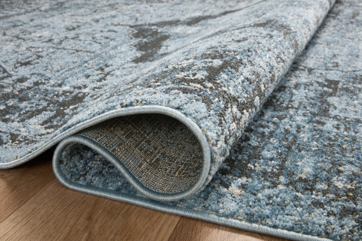 Rolled edge of blue-gray and charcoal distressed area rug with low-pile texture.