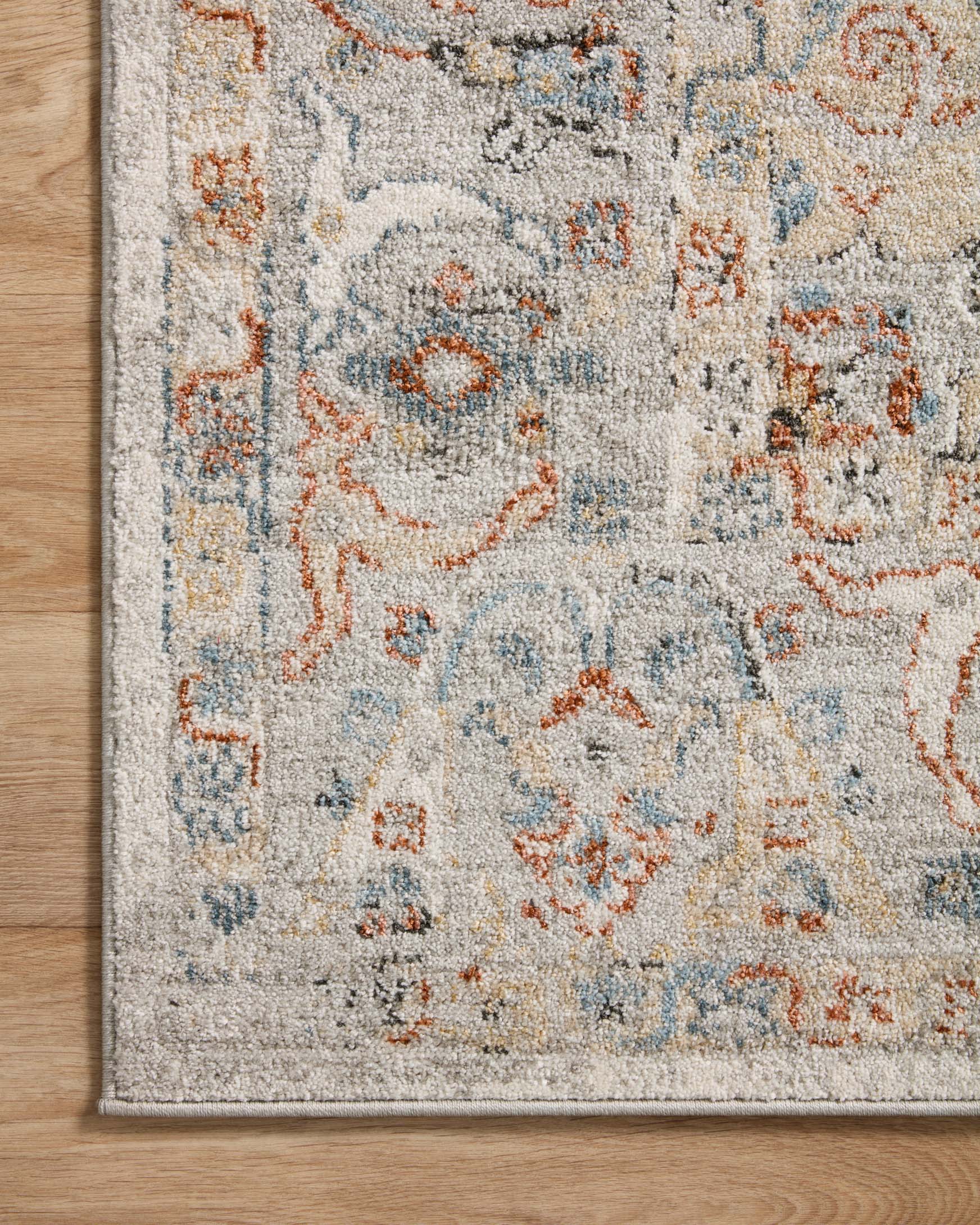 Ivory area rug with ornate blue and orange medallion and border motif, close-up.