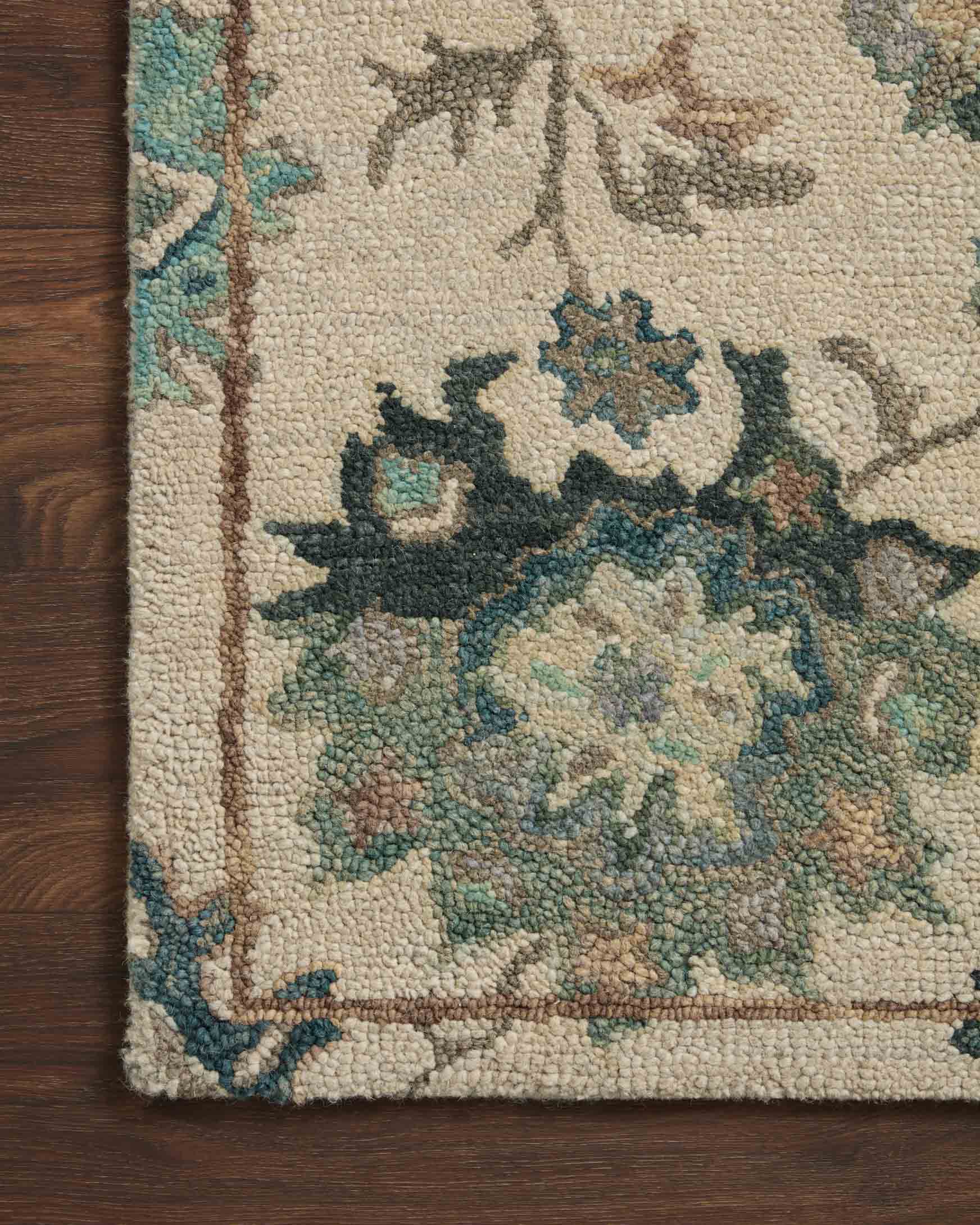Ivory area rug corner detail with teal, green, and dark motif embroidery texture