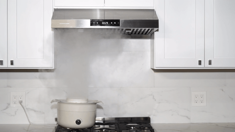 Under-cabinet black stainless range hood over a stove in a white kitchen setting