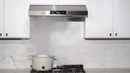 Stainless steel under-cabinet range hood with control panel and vent openings beneath.