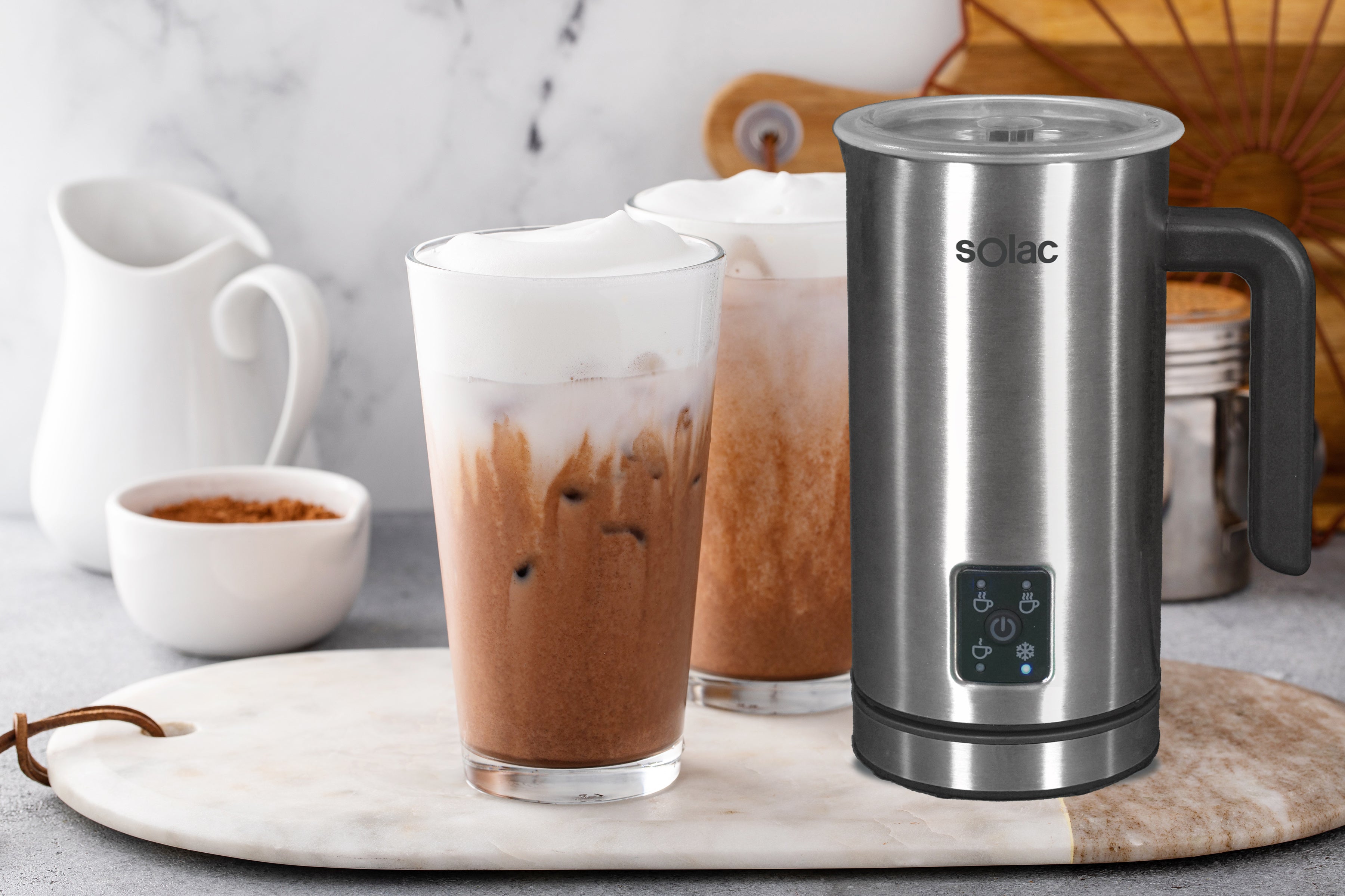 Stainless steel milk frother jug on counter near milk and hot chocolate cups