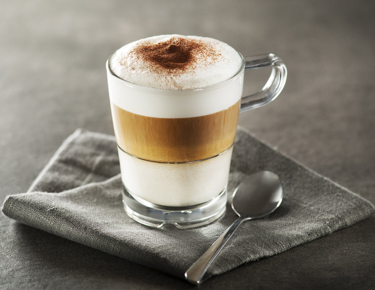 Stainless steel milk frother jug pouring foamy hot chocolate into a glass
