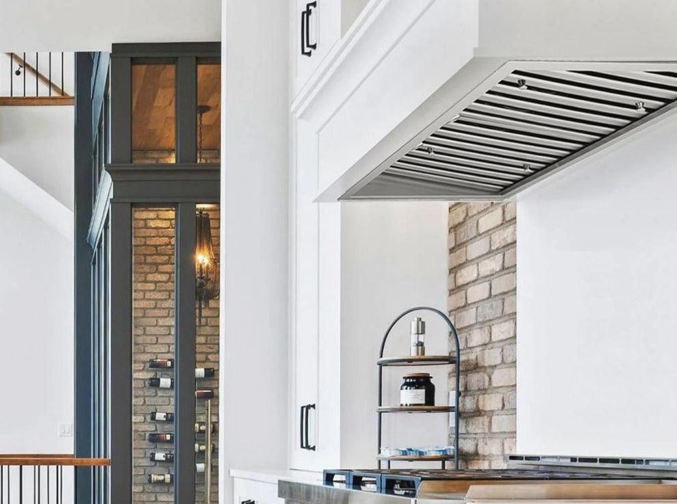 Stainless steel range hood insert mounted above cooktop, with vent baffle grille.