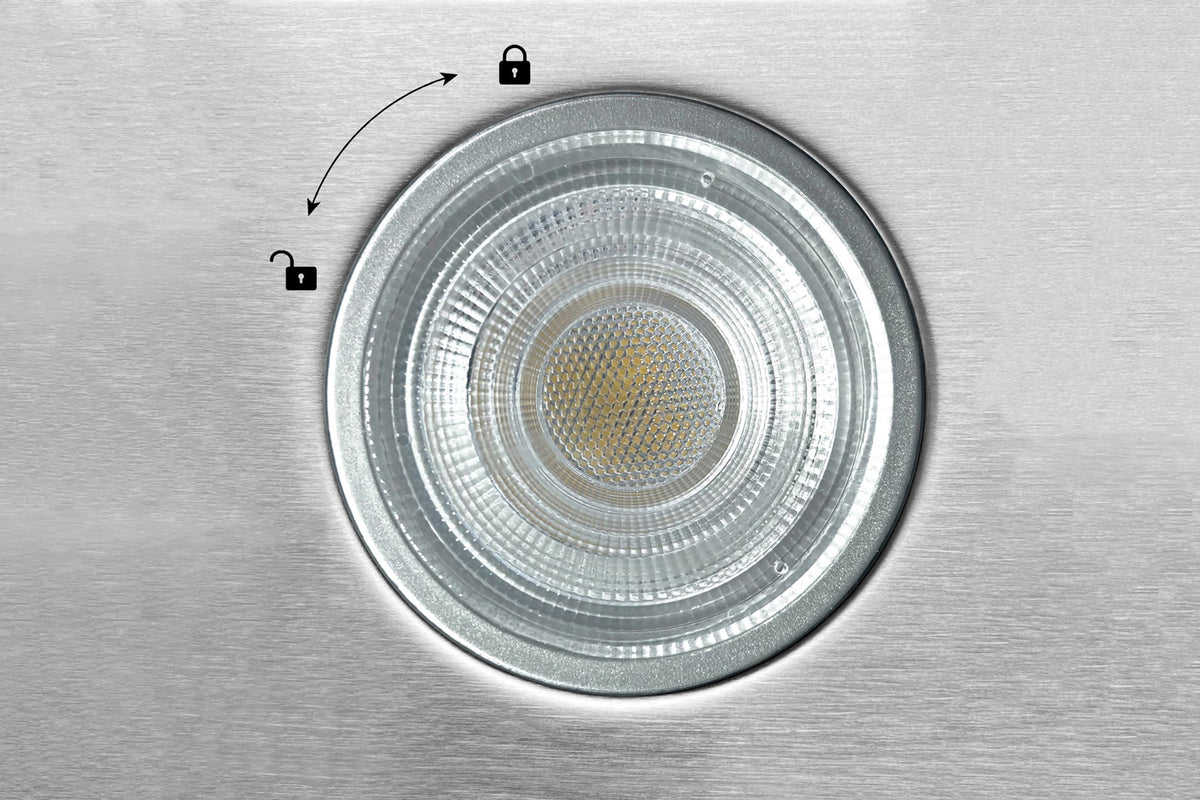 Circular stainless hood light lens on a brushed metal panel with small indicator icons.