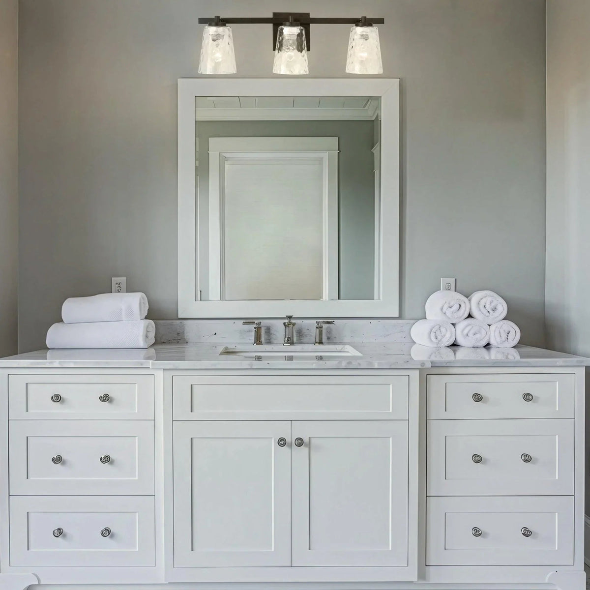 Three-light vanity light with clear textured glass shades and dark mounting bar
