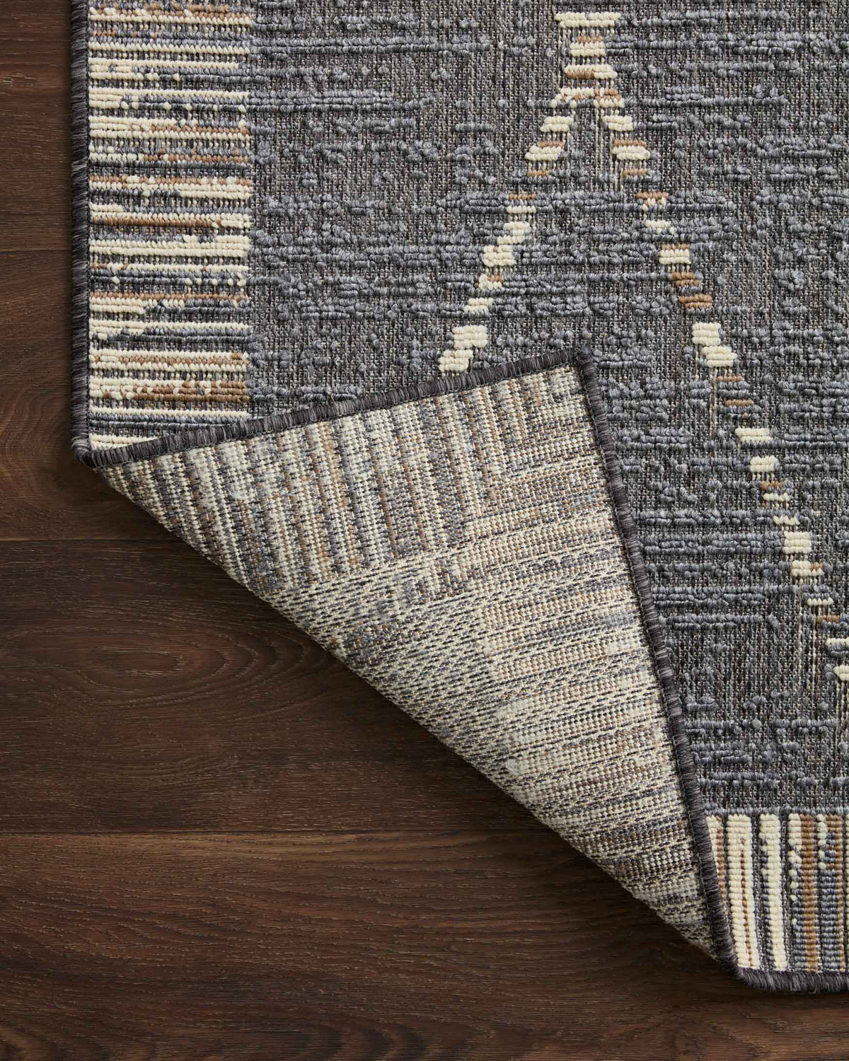 Bottom corner of slate gray rug with reverse weave and striped cream accents.