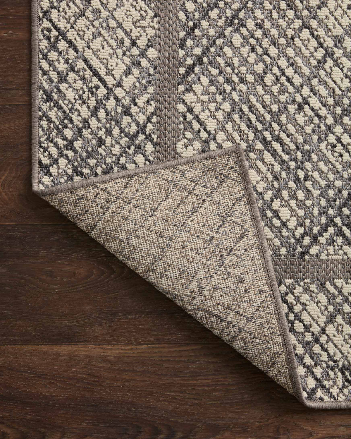 Corner view of indoor/outdoor accent rug in ivory and charcoal with diamond pattern border