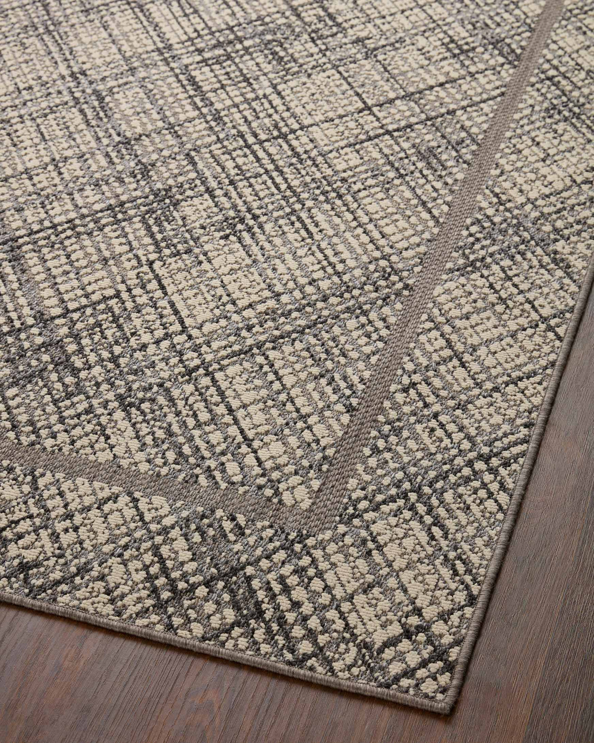 Ivory and charcoal indoor/outdoor rug with subtle grid and diamond pattern on dark backing