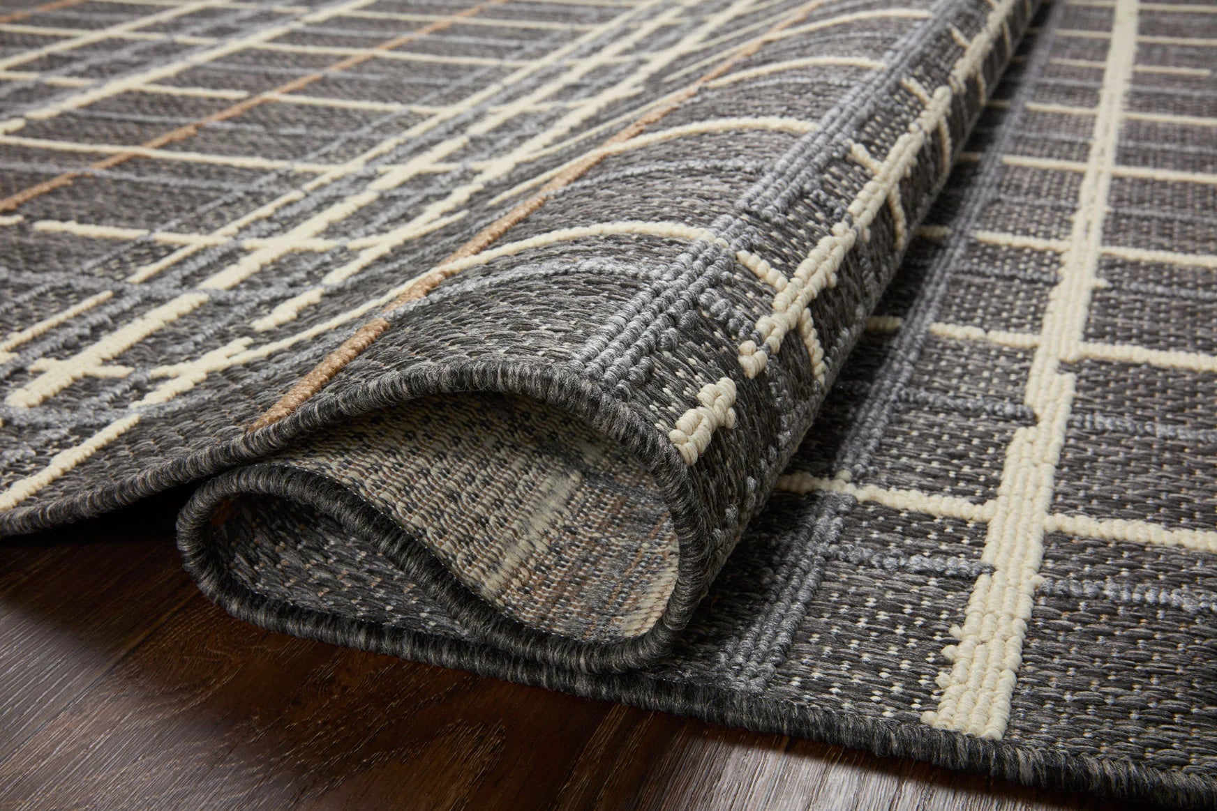 Charcoal rug corner with rolled edge; cream grid lines and tan highlights