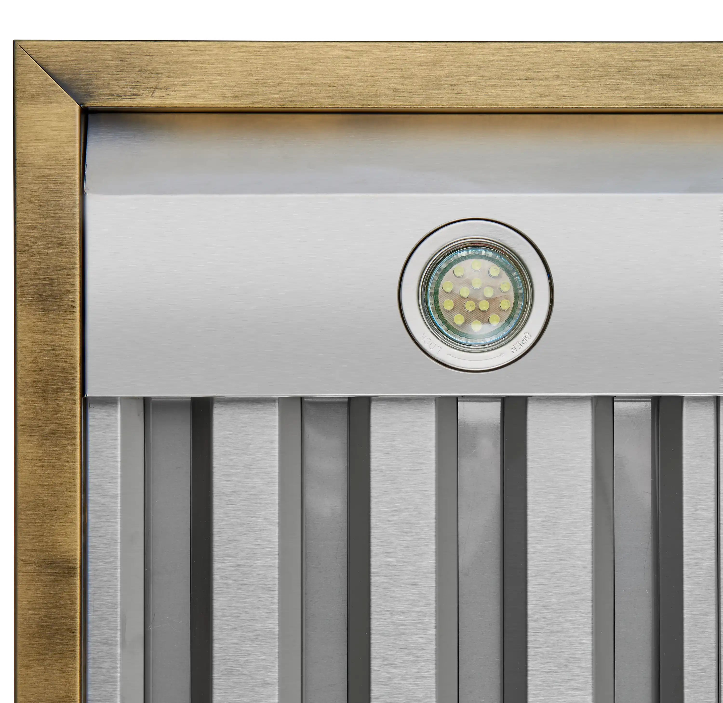 Range hood side vent with round LED lens and antique brass frame over grille.