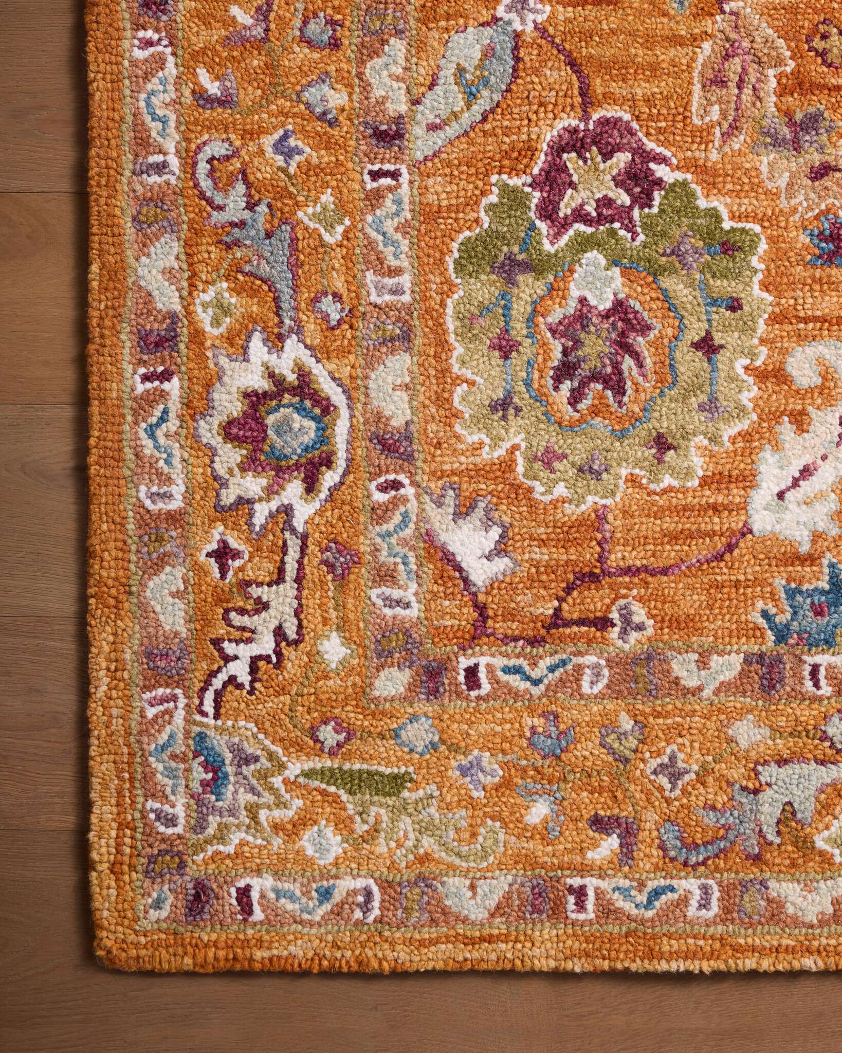 Corner close-up of orange hooked rug with floral motifs and blue accents