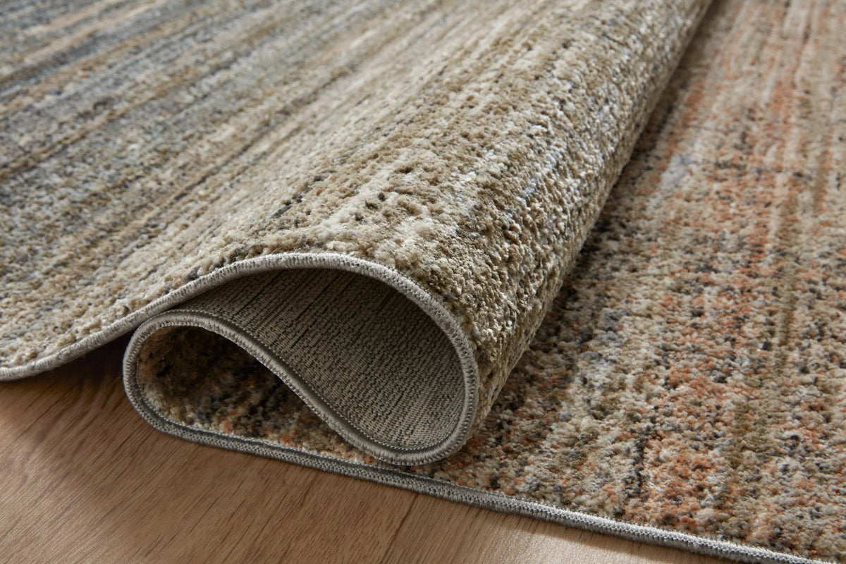 Area rug corner shown rolled; textured weave with blue-gray and beige flecked stripes