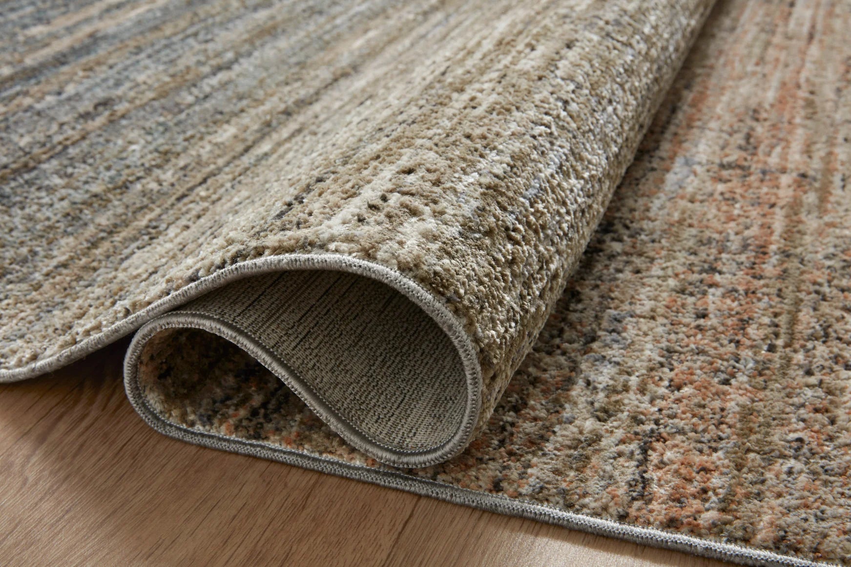Rolled-up beige, blue, and gray area rug with textured low-pile edge.