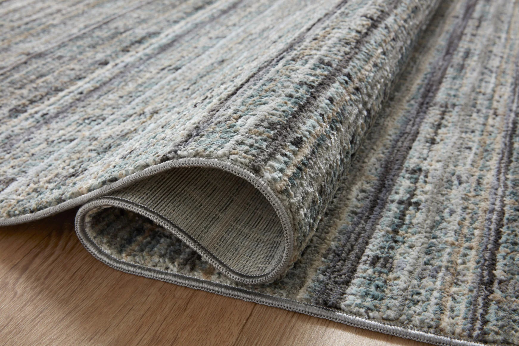 Gray-blue area rug edge with bound border and mottled woven texture closeup