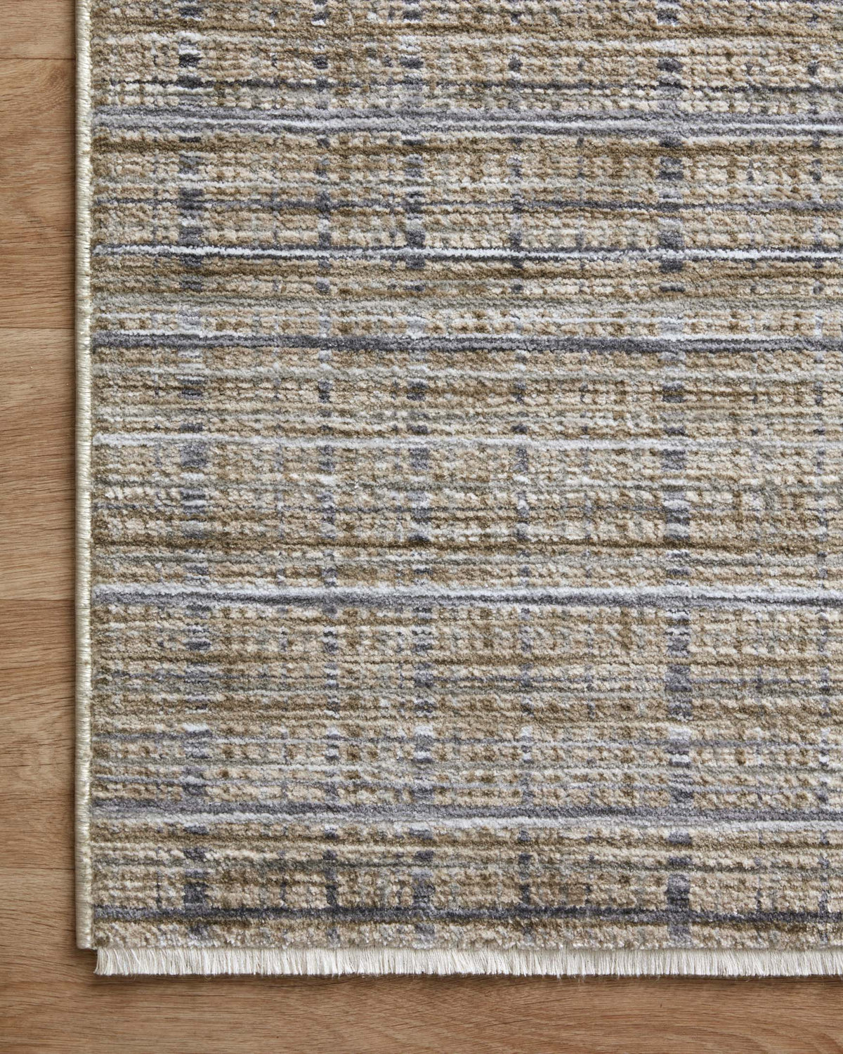 Corner view of beige and charcoal area rug with distressed stripe texture and bound edge