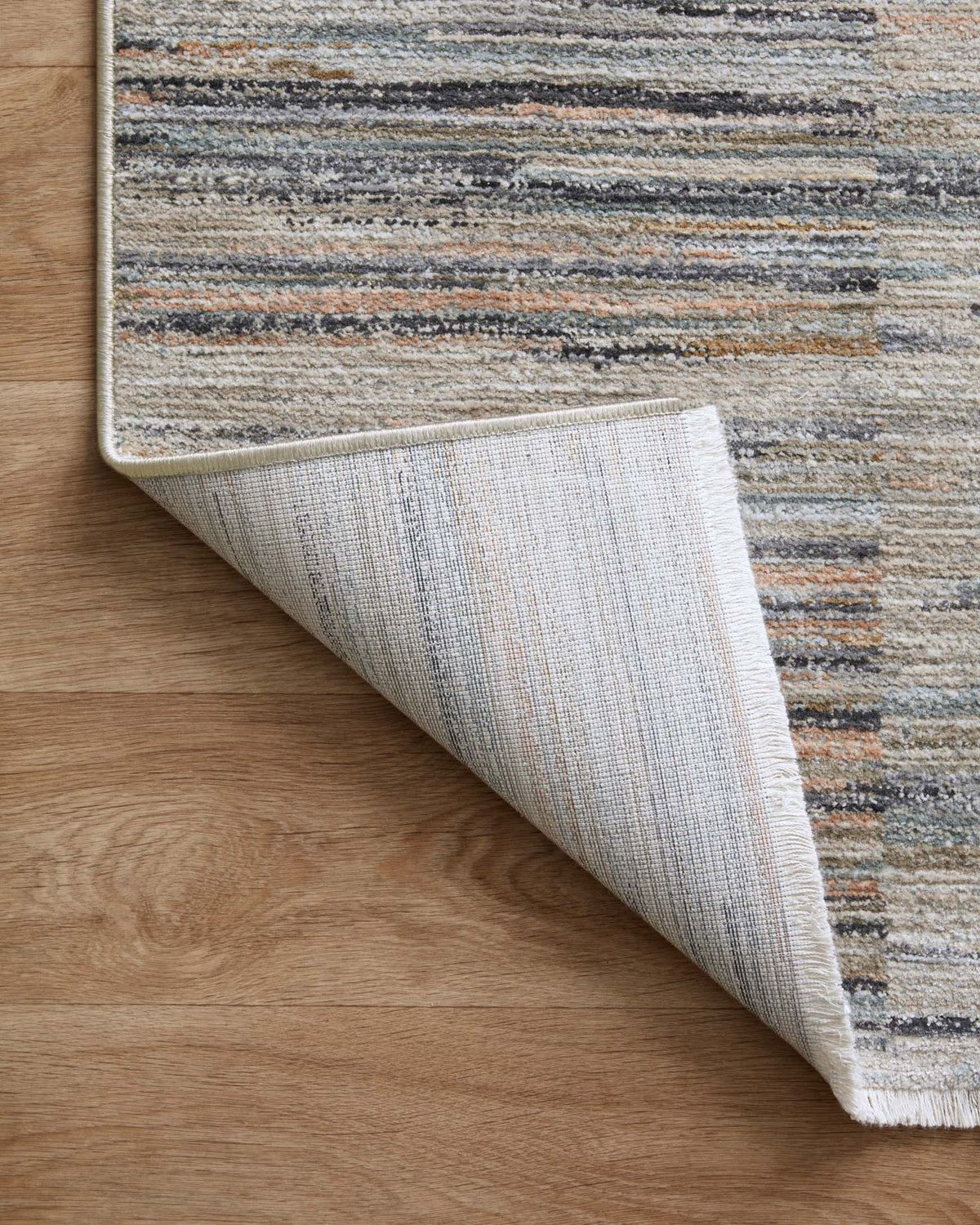 Accent rug corner rolled back to show underside backing and woven stripe construction.