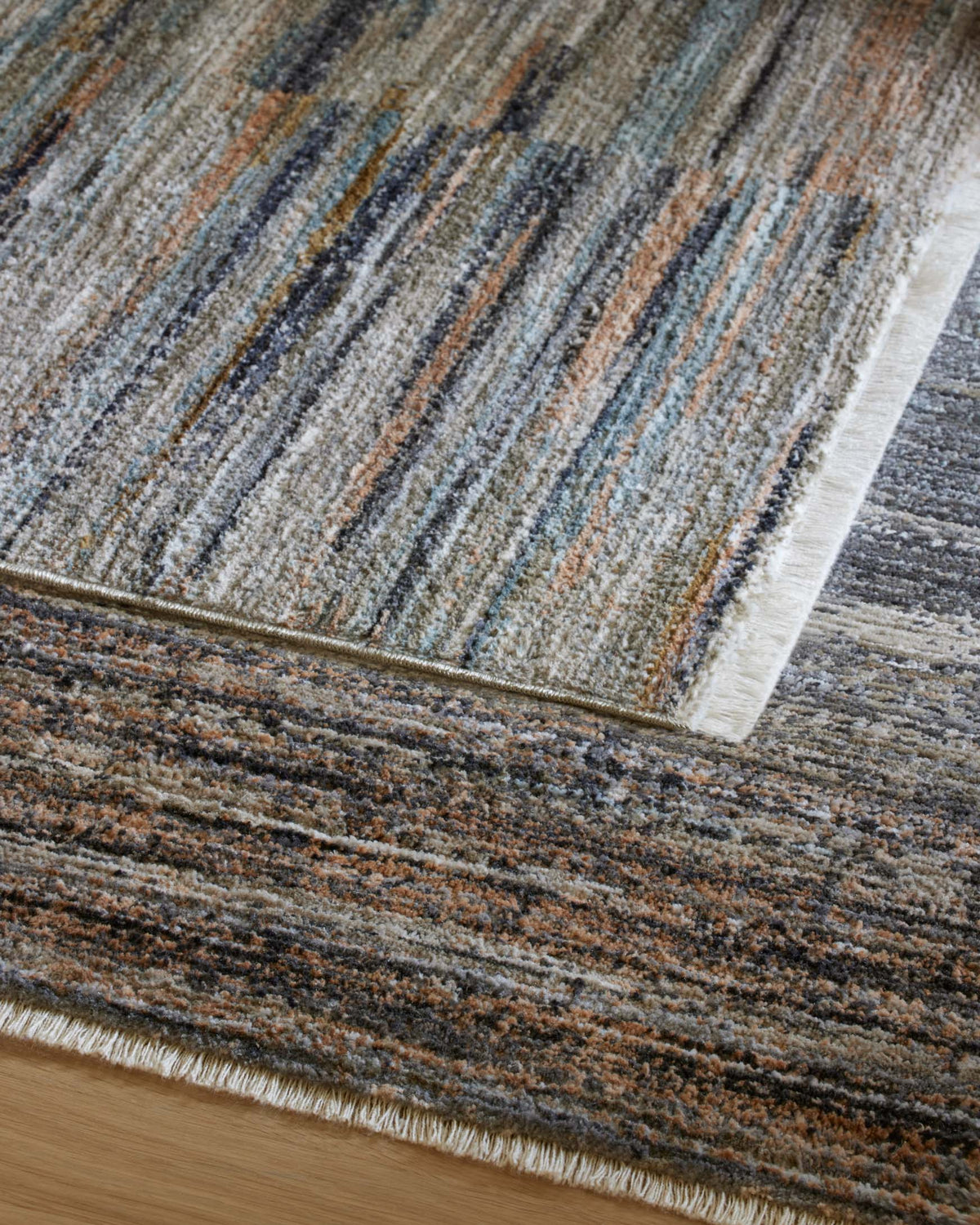 Area rug with layered multicolor stripes in gray, blue, and brown tones and short fringe edge.
