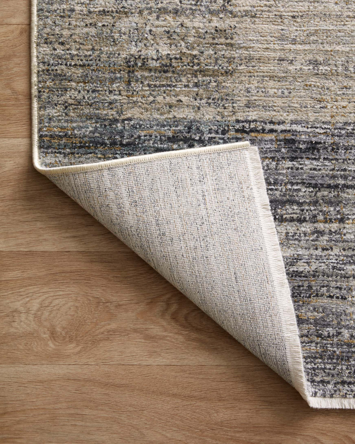 Corner close-up of grey and gold abstract area rug with woven backing and folded edge
