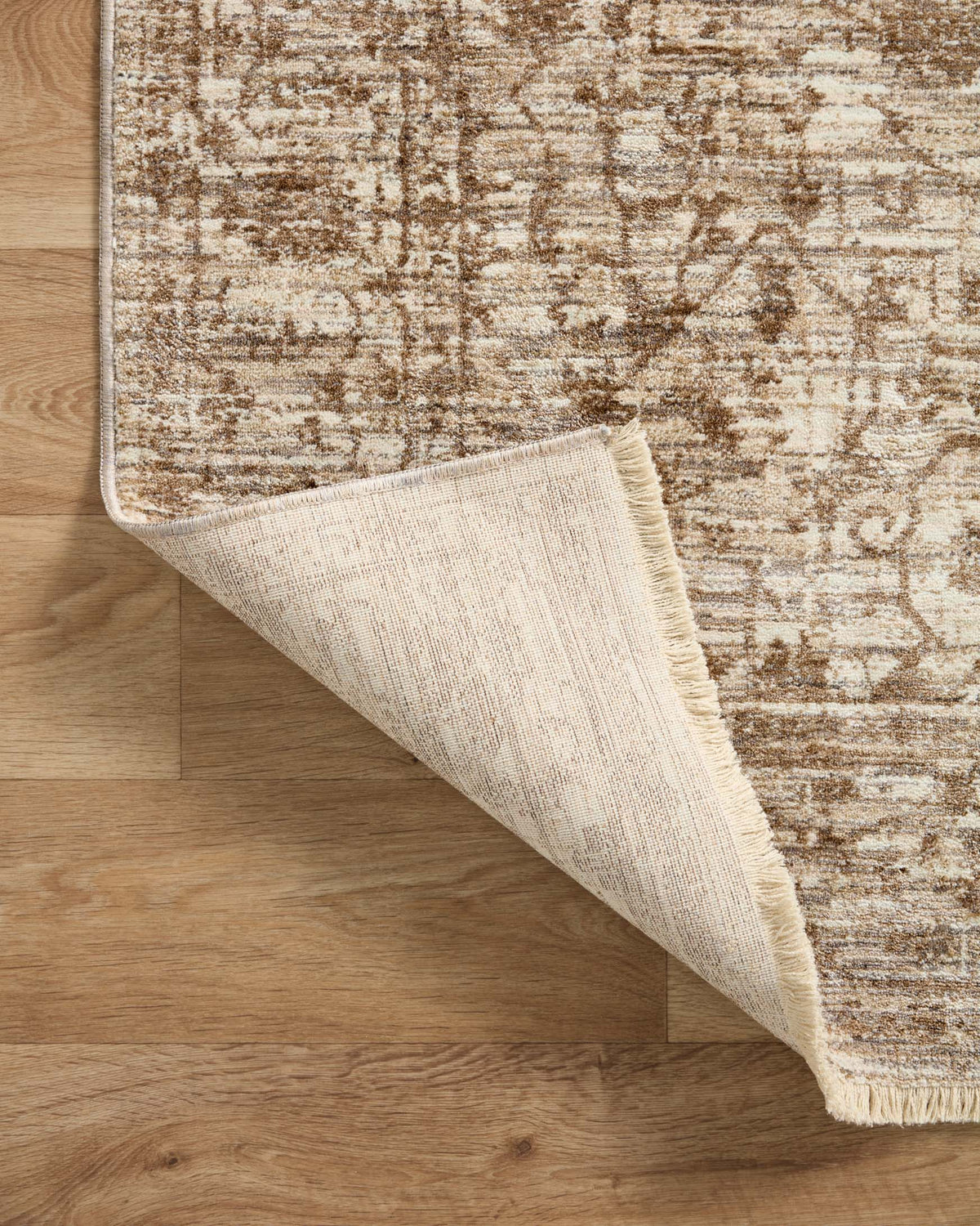 Traditional rug corner lifted to show cream underside weave and short fringe
