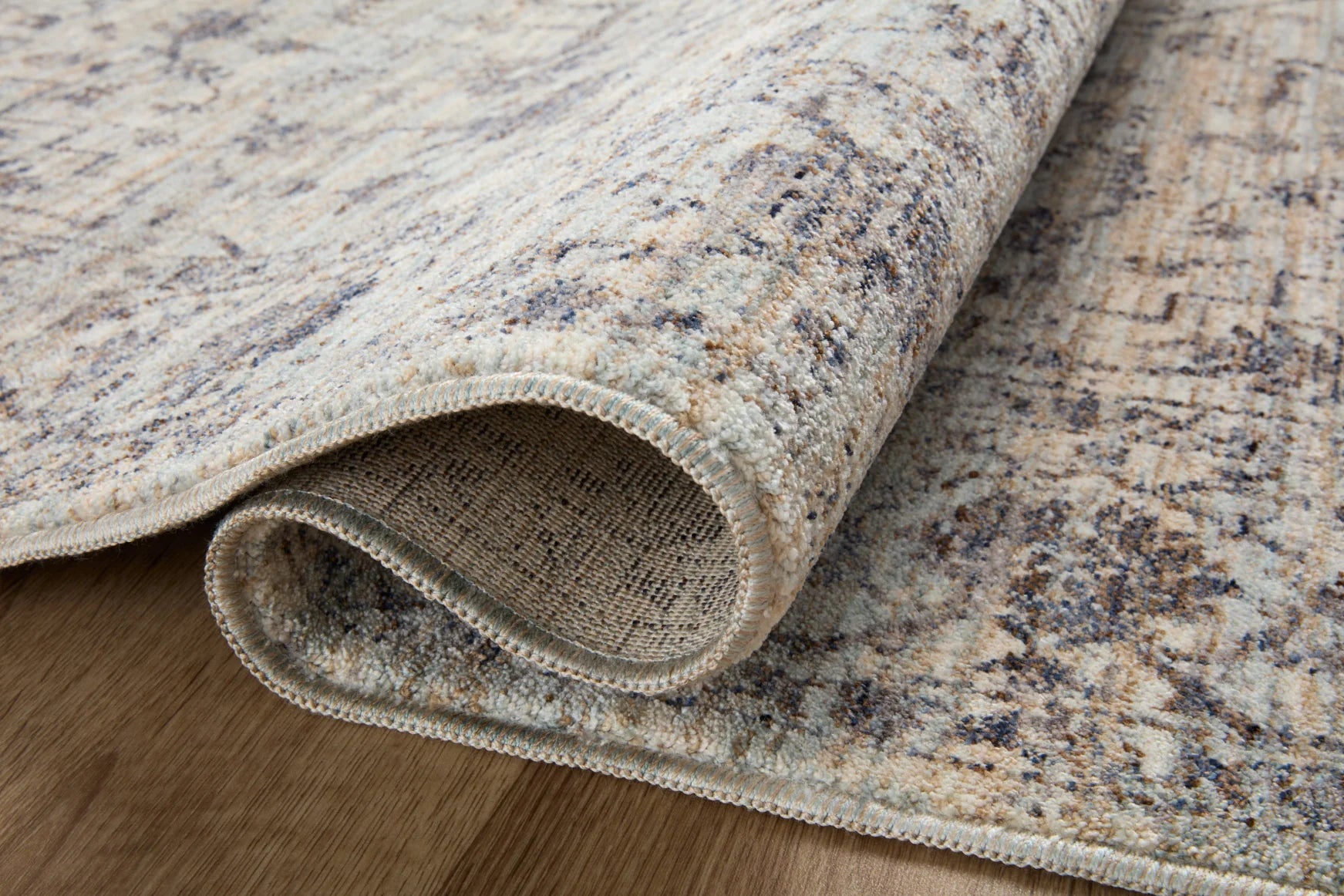 Traditional area rug rolled edge detail in mist and charcoal with stitched border.