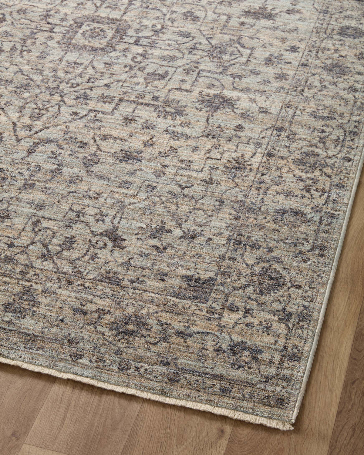 Close-up of traditional area rug pattern in mist, tan, and charcoal with distressed texture.