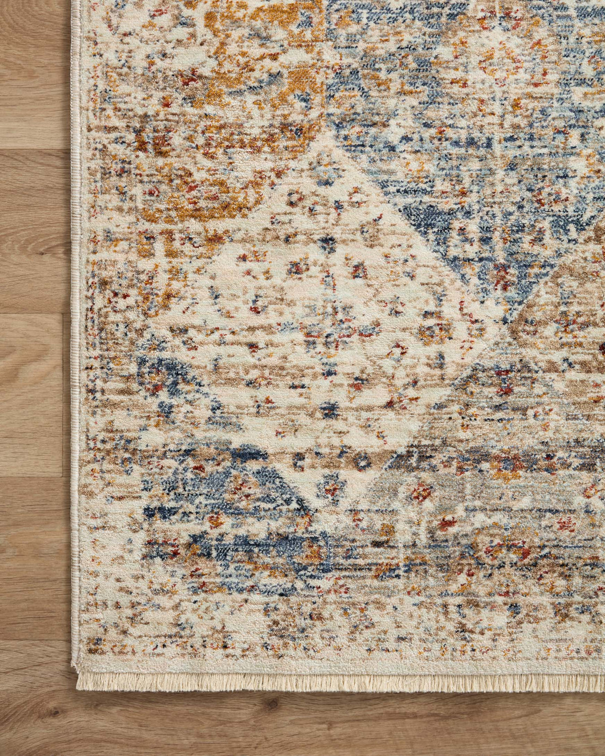 Corner view of area rug with ivory base, distressed blue and rust diamond pattern, fringed edge