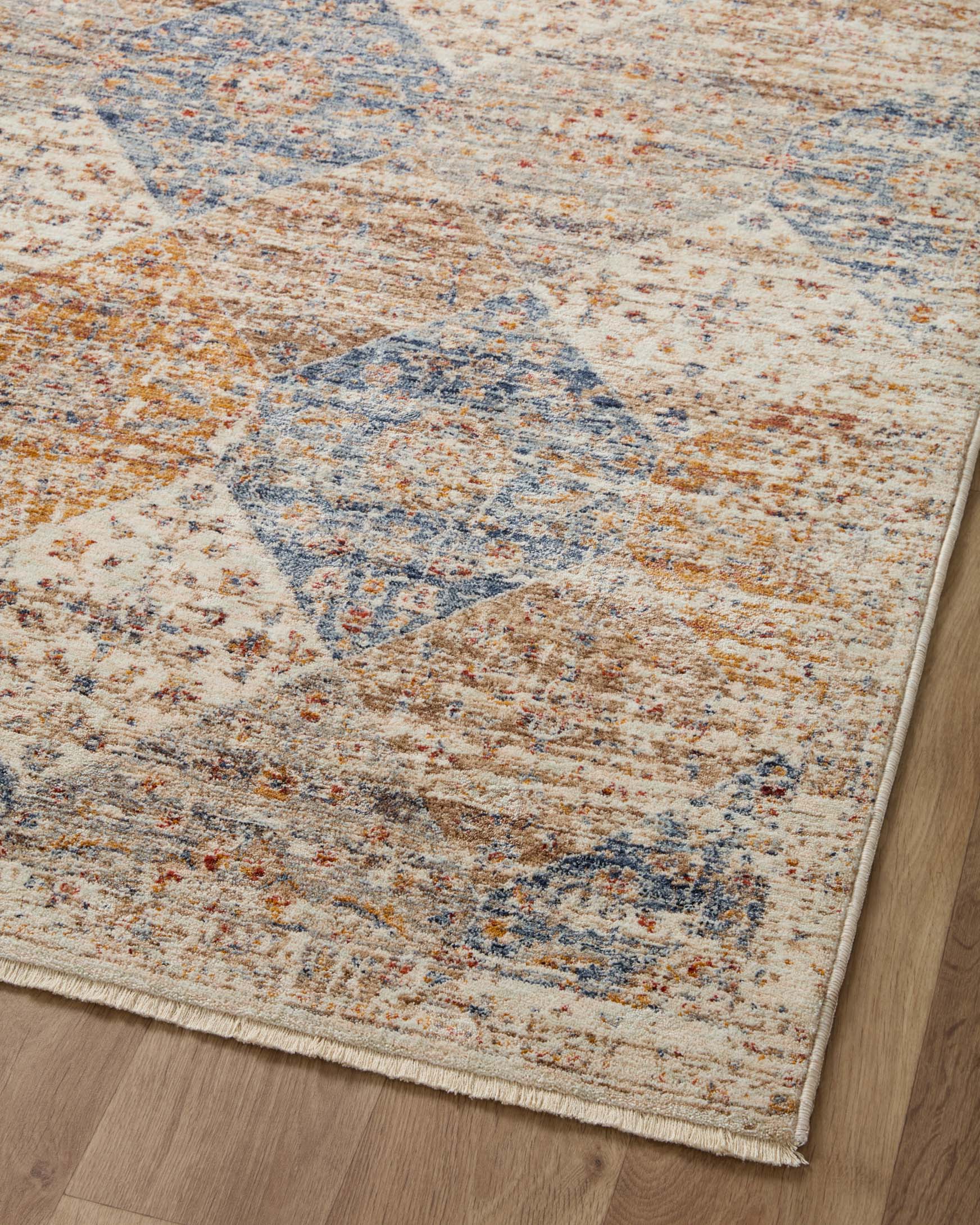 Area rug angled on wood floor with ivory base, scattered blue and rust diamond motifs