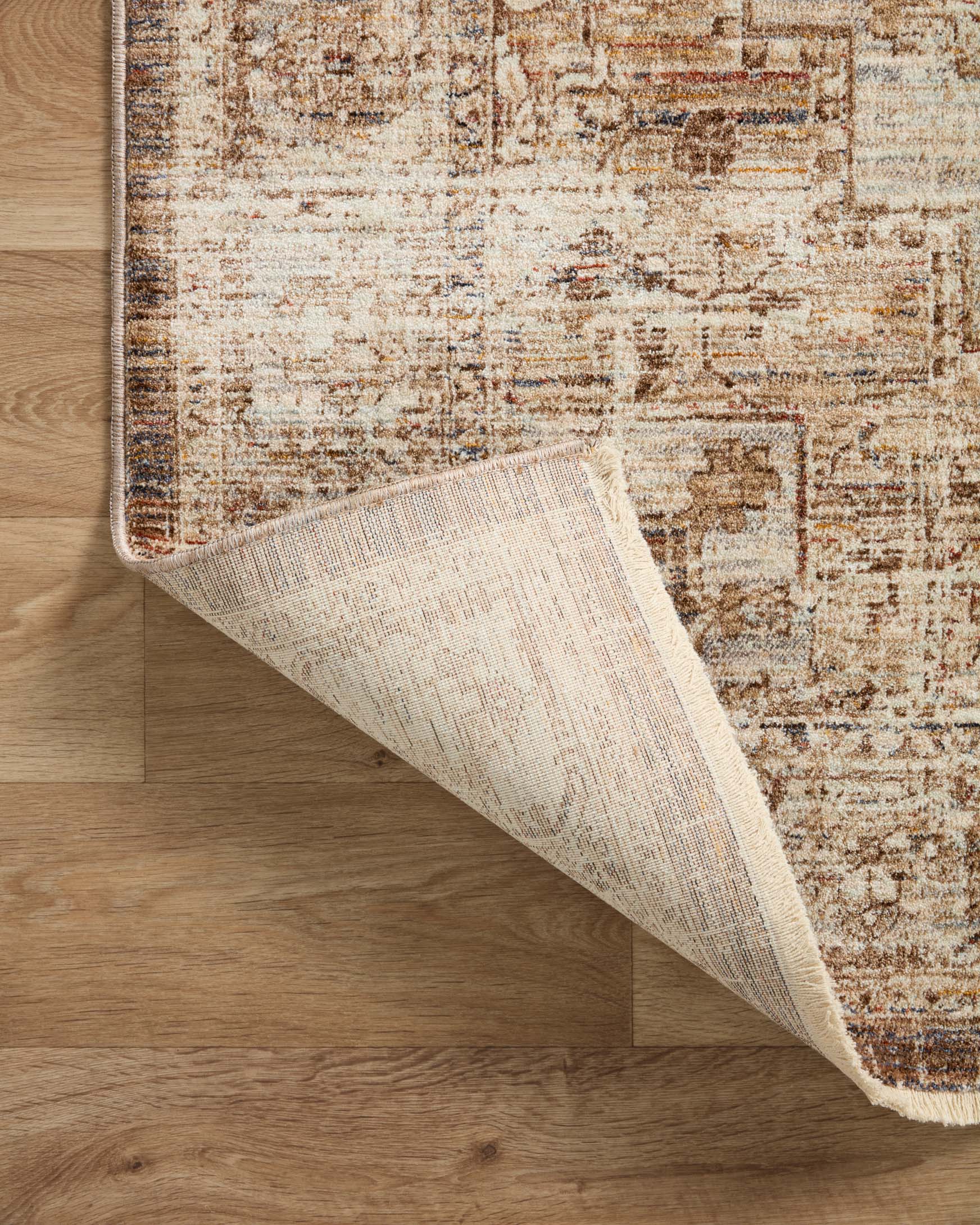 Rolled corner of beige and mocha rug on wood floor, showing underside texture.