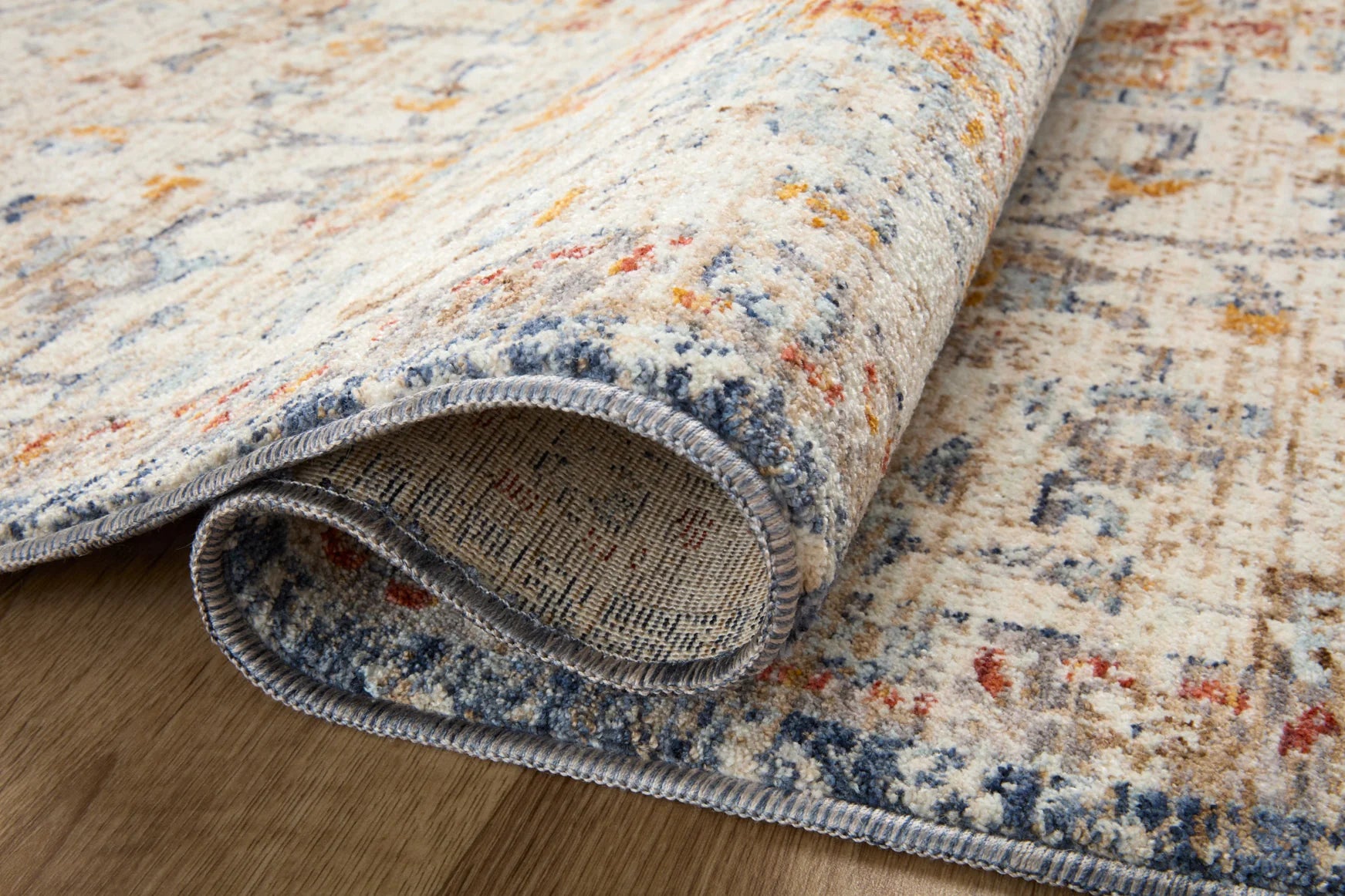 Ivory rug edge close-up with navy binding and mottled blue, orange, rust pattern.