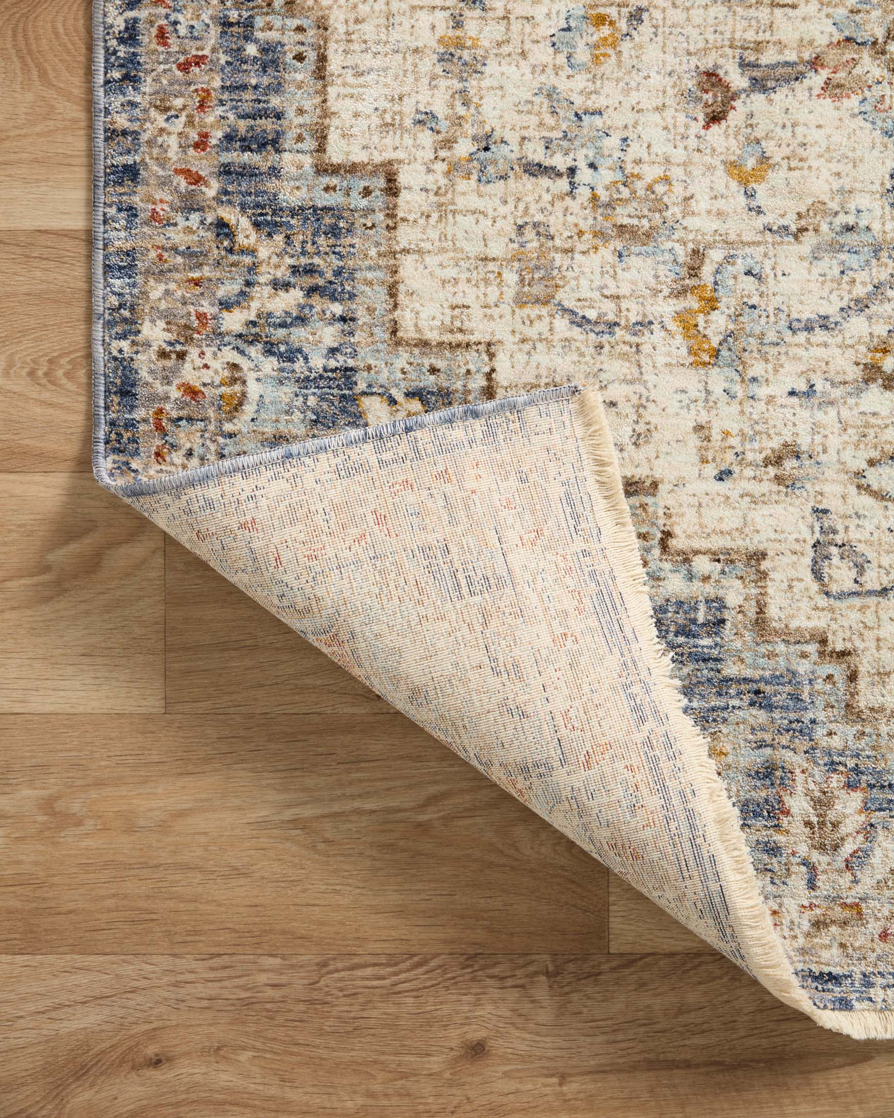 Ivory rug corner detail with navy edging, rug backing, and blue-orange distressed pattern.