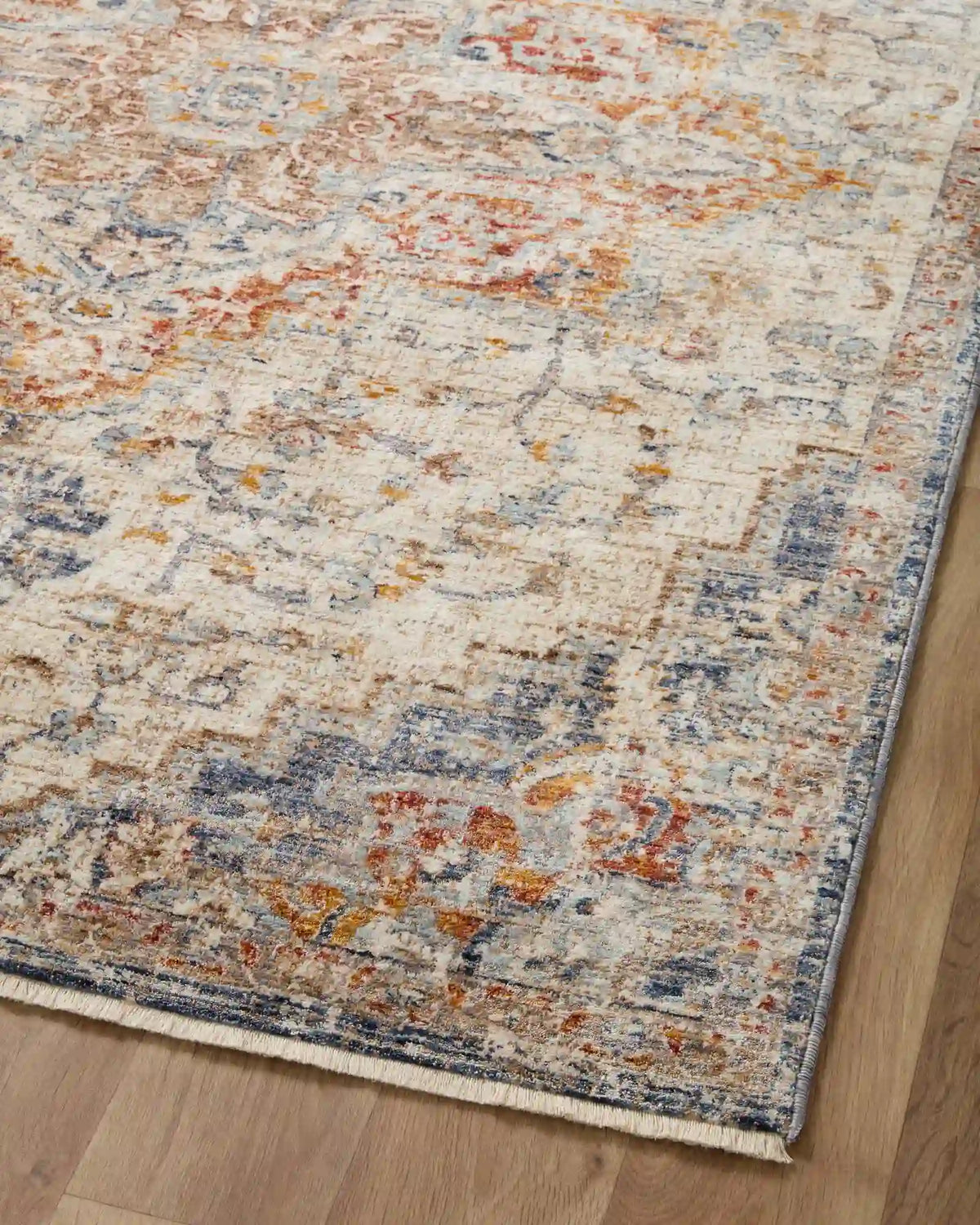 Distressed traditional rug in ivory with speckled blue and rust/orange motifs and blue border.