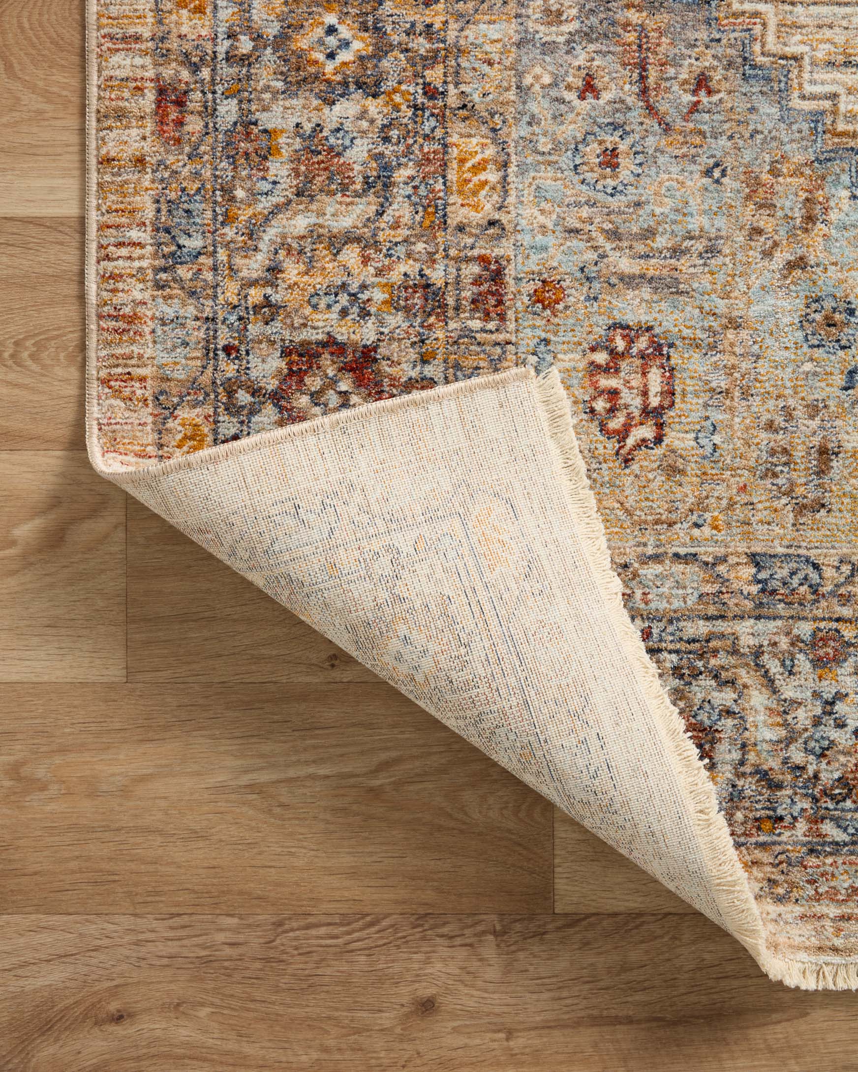 Traditional rug corner showing light underside backing and multicolor distressed pattern, fringed