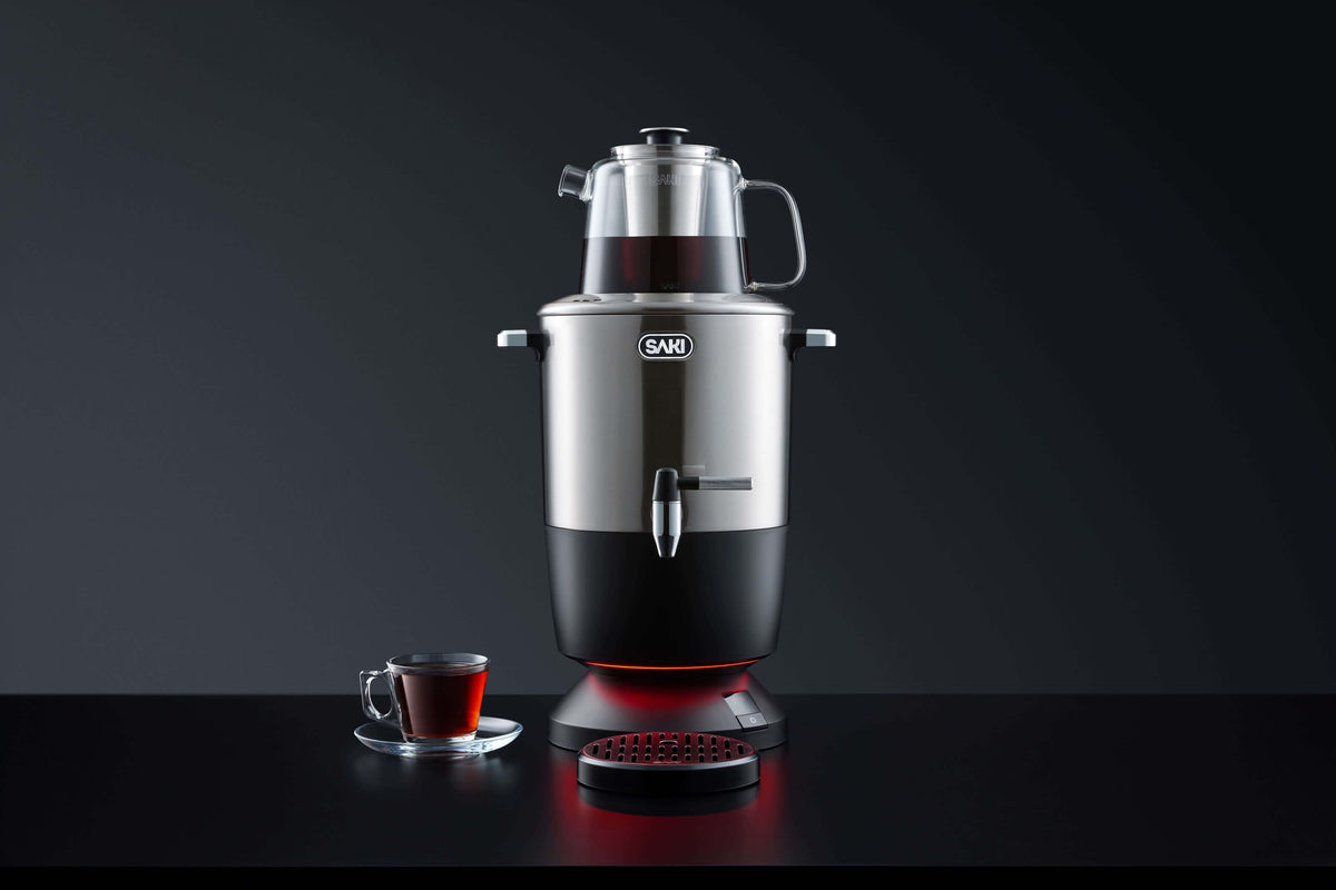 Silver electric tea maker with black body and base, set with a small tea cup.