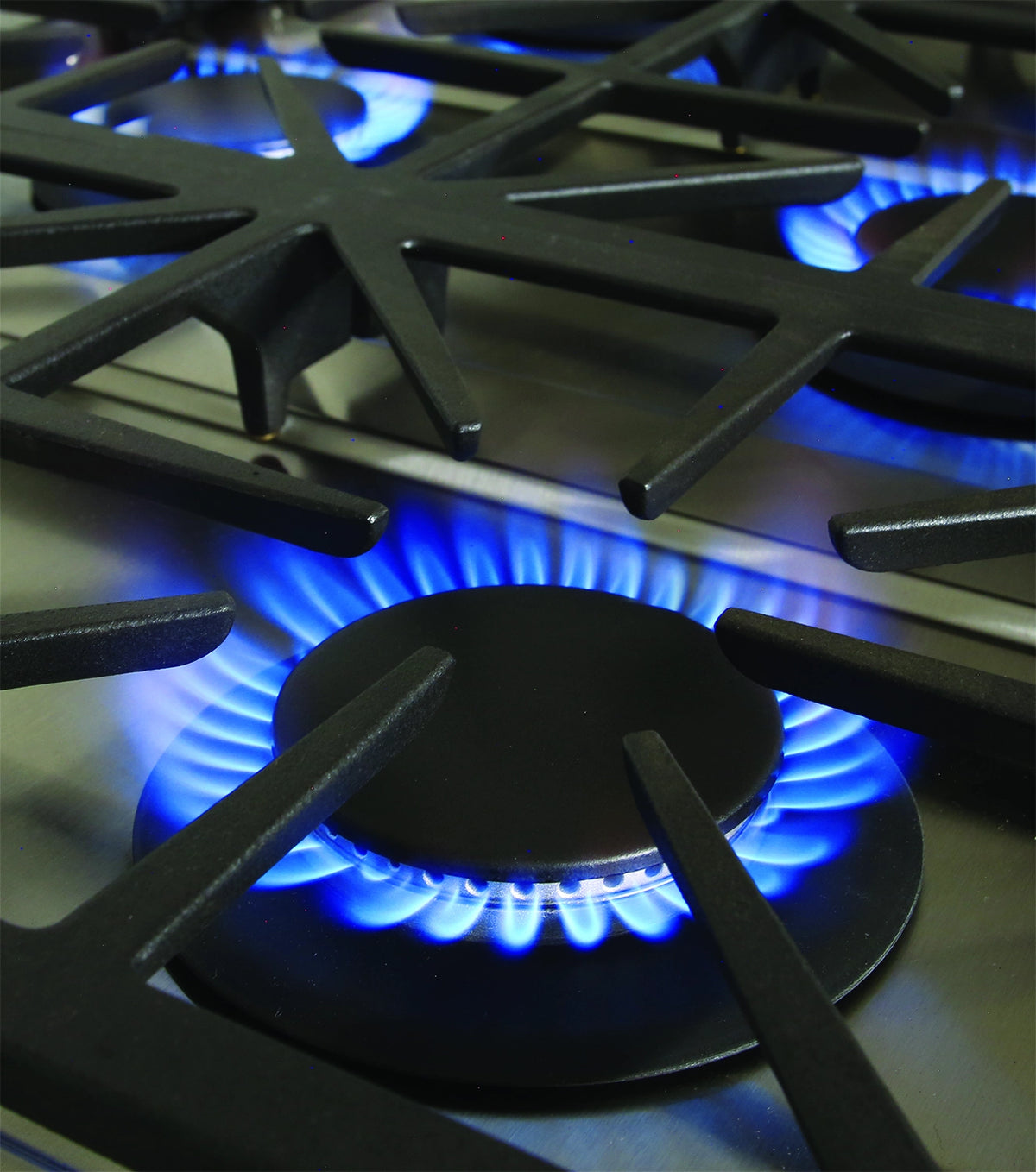 Gas burner grate with blue flame on a stainless gas range cooktop