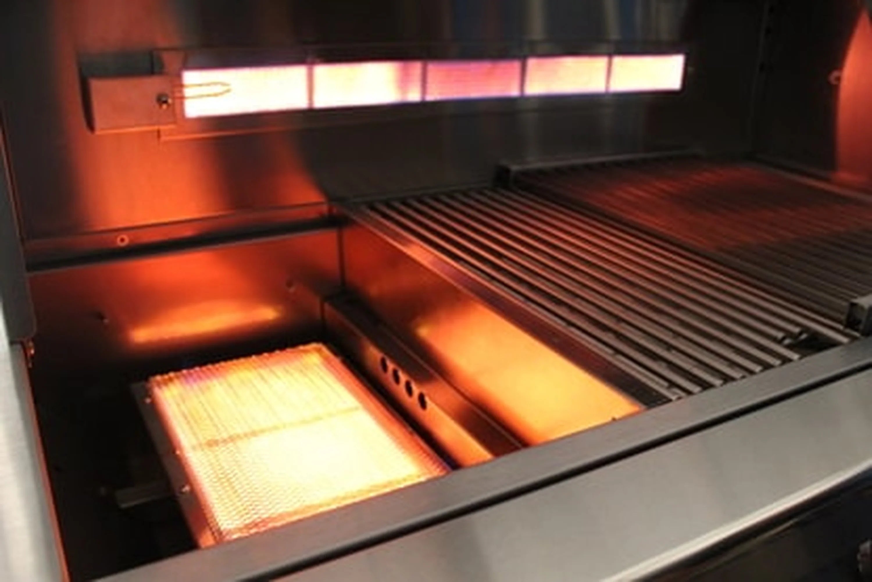 Gas grill firebox with glowing burners and cooking grates under heat