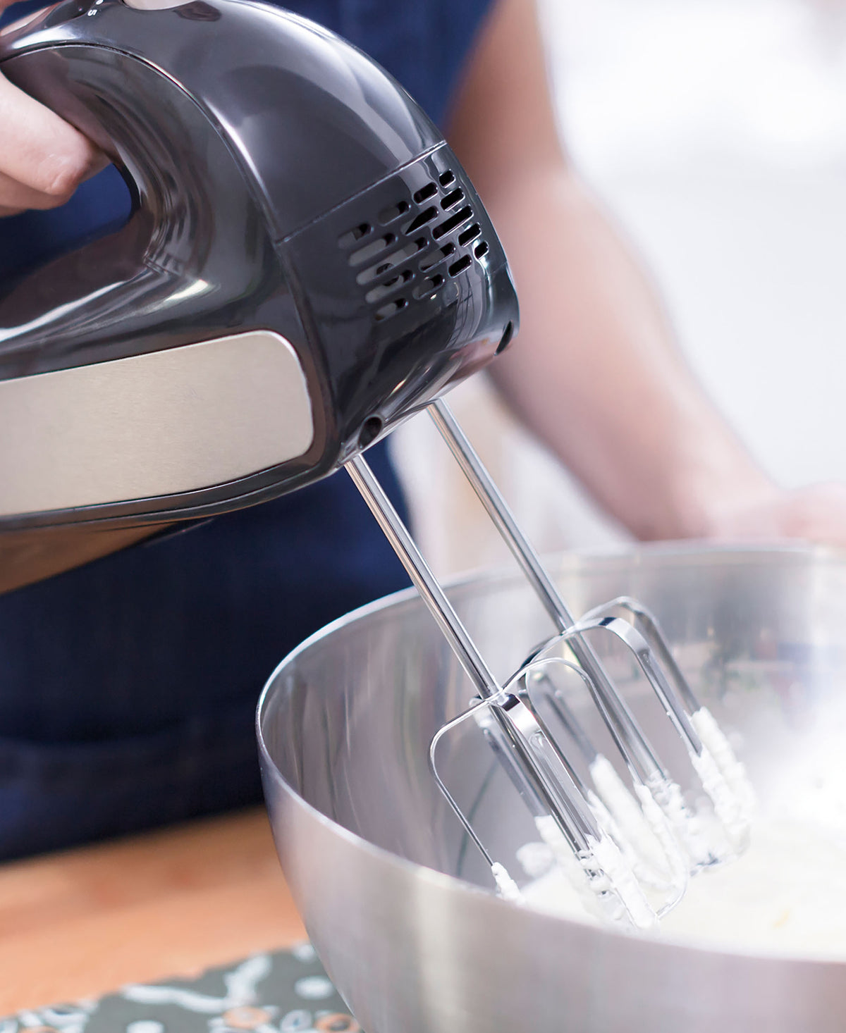 Chrome beaters whipping batter in a bowl with a black hand mixer.