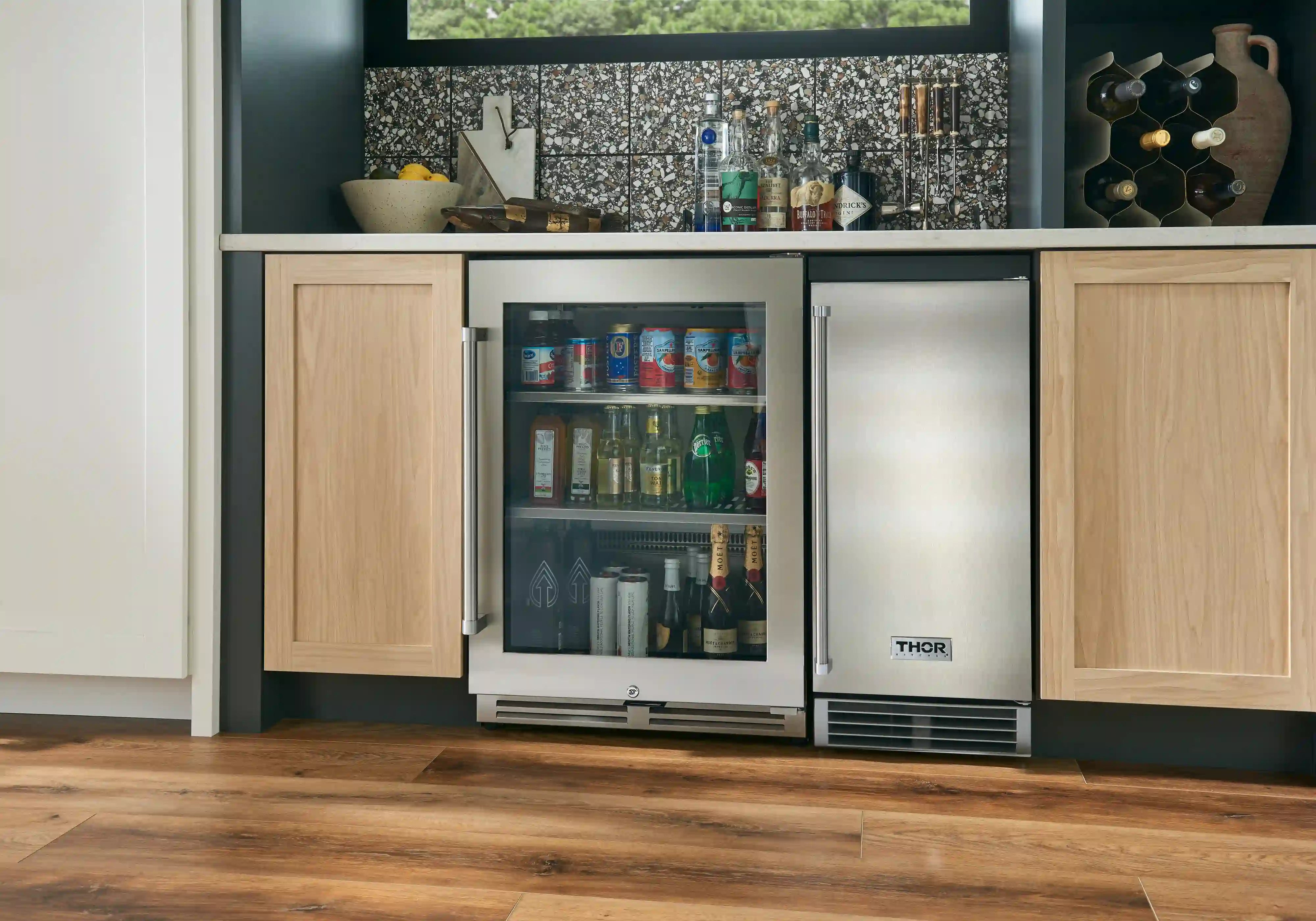 Undercounter beverage cooler with glass door installed in kitchen, stocked with bottles