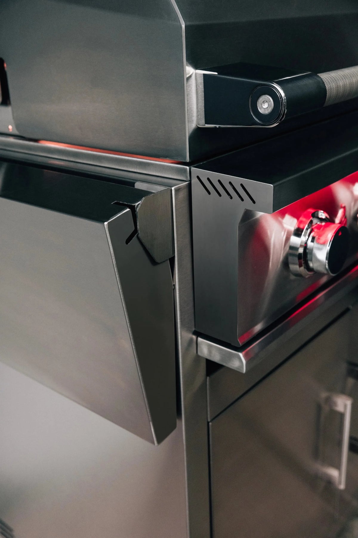 Stainless grill side burner area with control knob and red heating elements.