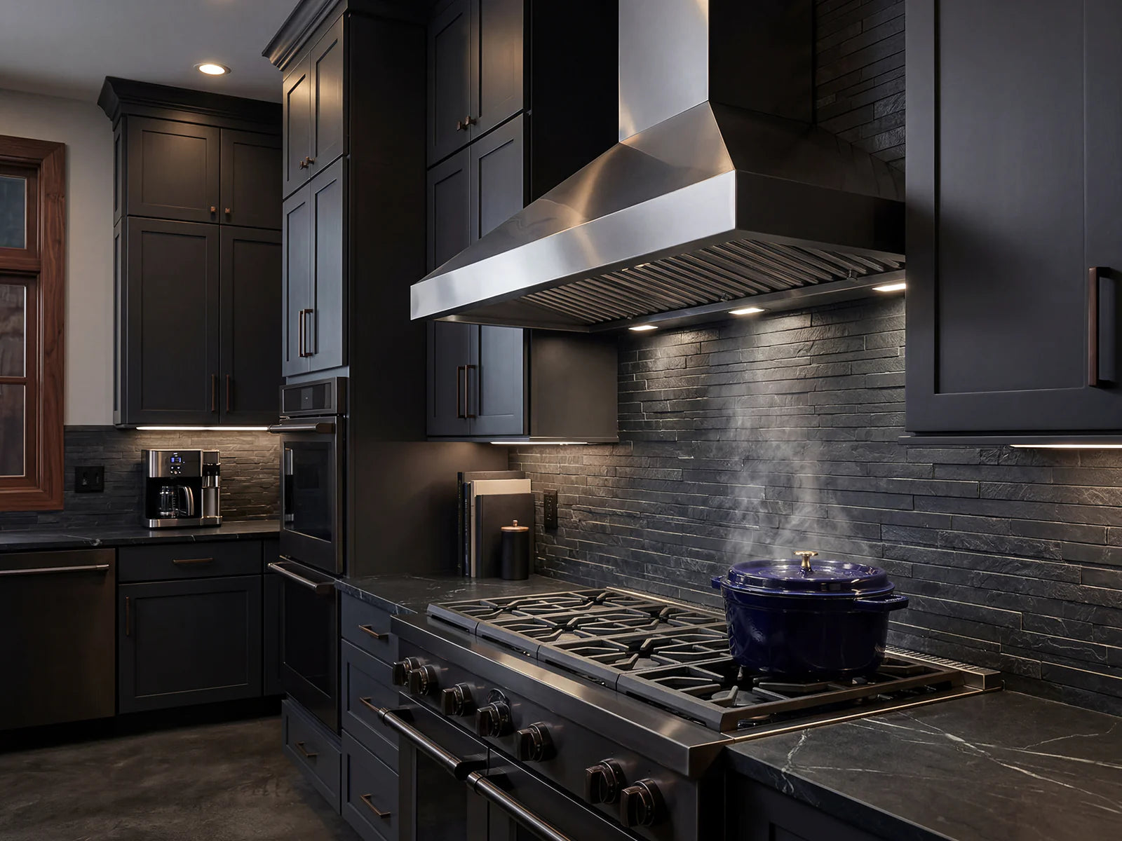 Stainless steel wall range hood over a gas cooktop with bright underside vent lights