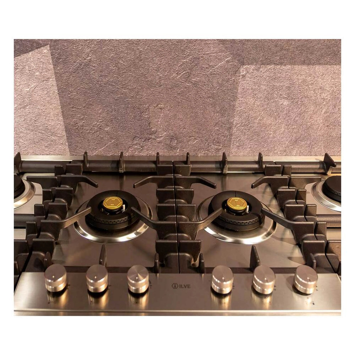 Gas burner grates and brass burner caps on a stainless steel cooktop surface.