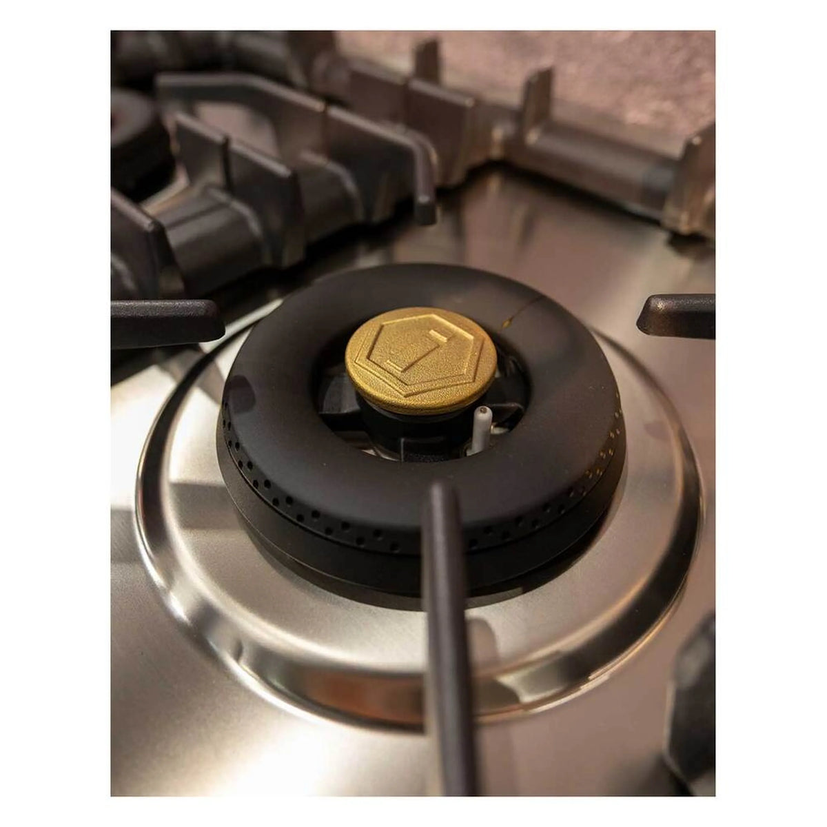Single gas burner on a stainless steel cooktop with black grate and brass cap.